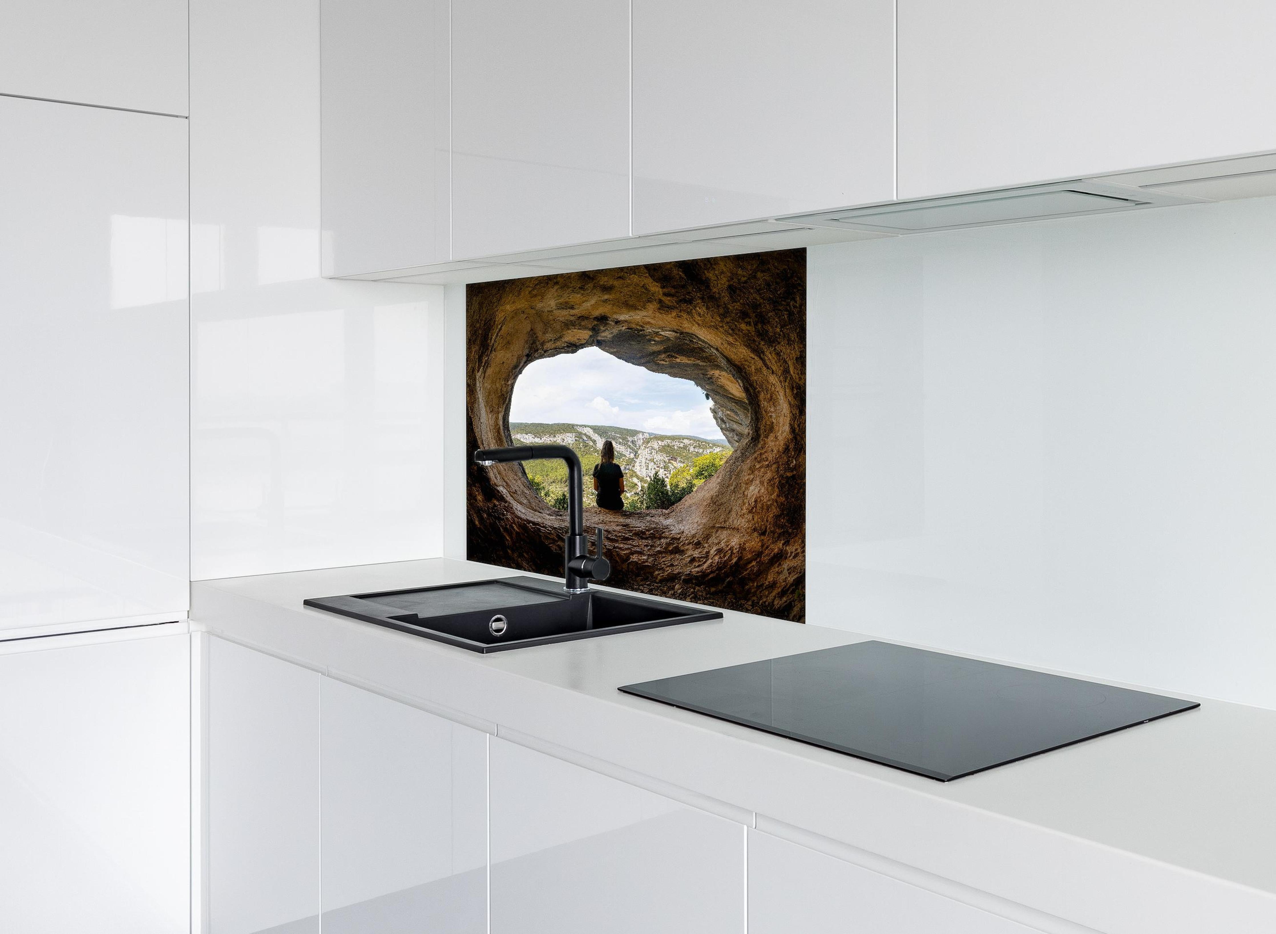 Spritzschutz - Frau sitzend in Berghöhle mit Blick auf Landschaft hinter einem Cerankochfeld zwischen Holz-Kochutensilien