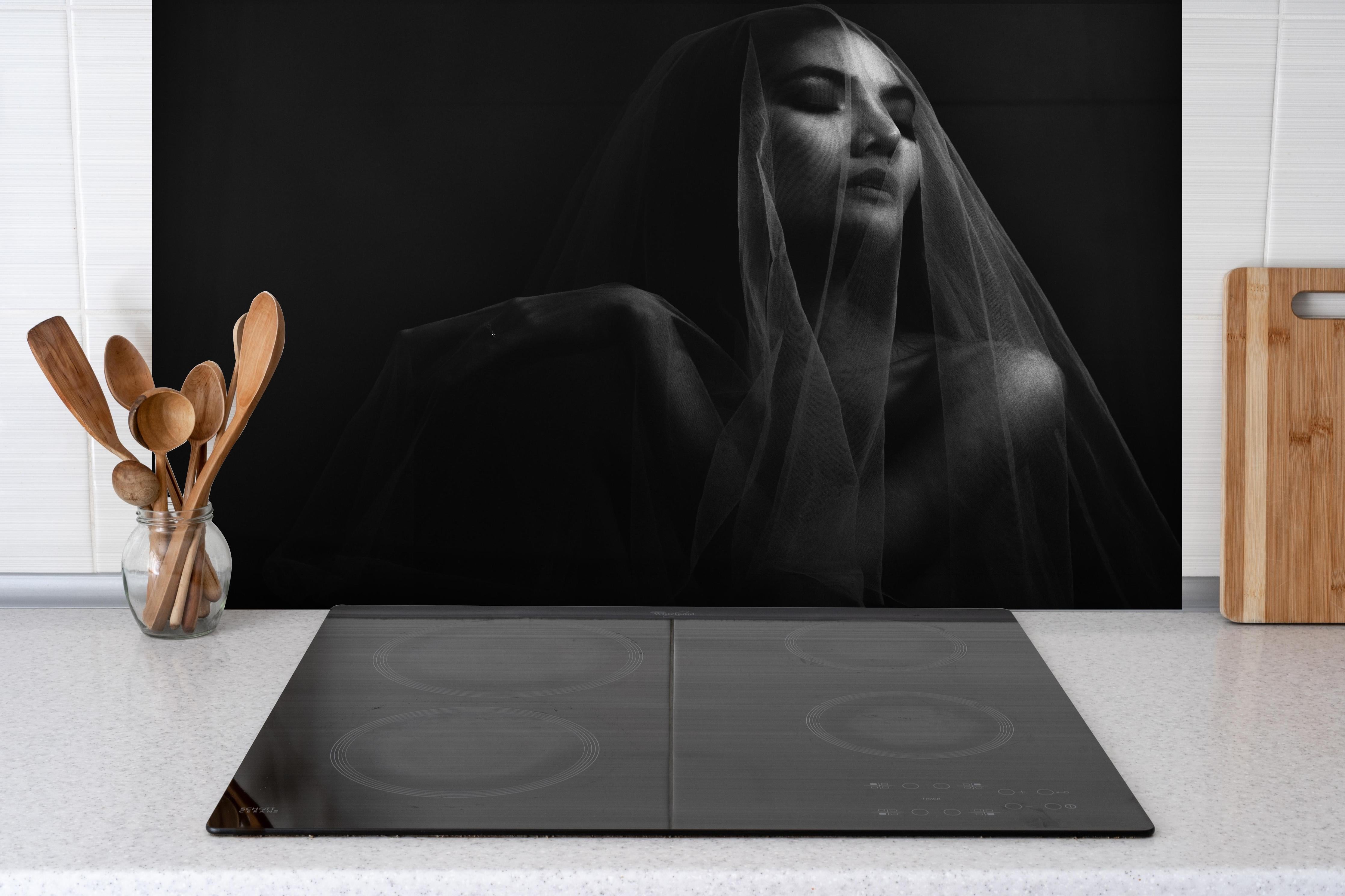 Spritzschutz - Frau unter einem Schleier im dunkeln hinter einem Cerankochfeld zwischen Holz-Kochutensilien