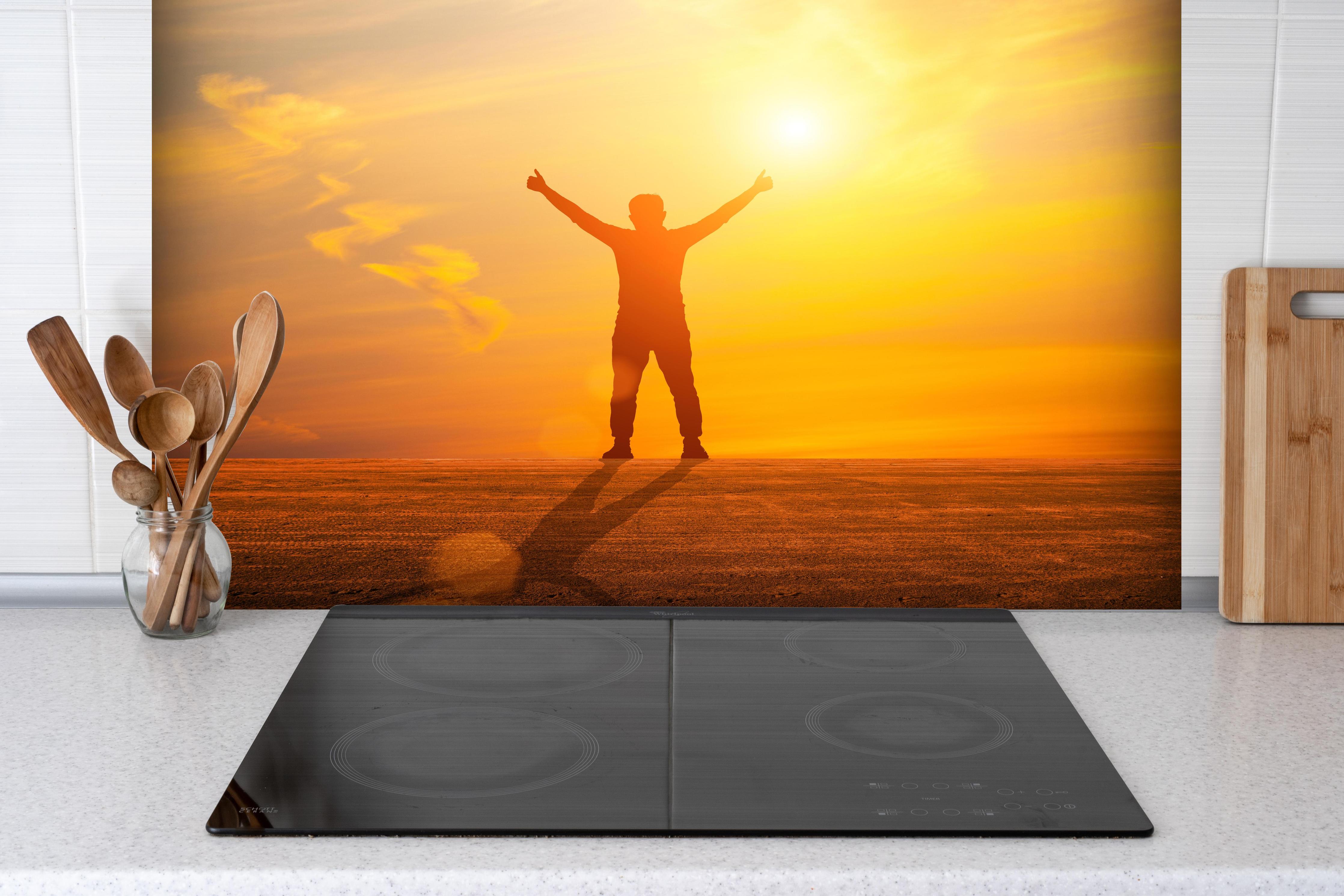 Spritzschutz - Freier Mann im goldenen Licht der Sonne hinter einem Cerankochfeld zwischen Holz-Kochutensilien