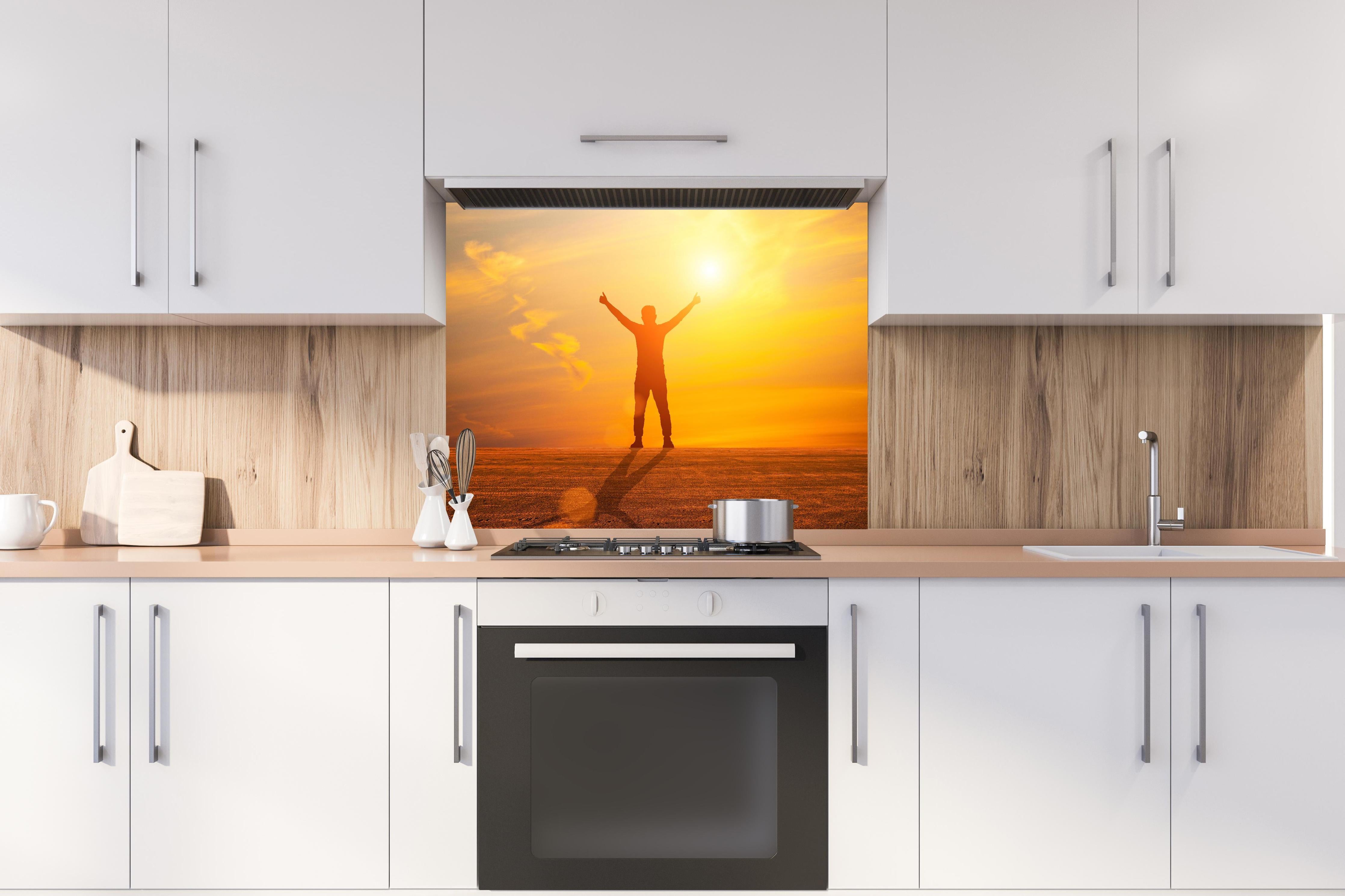 Spritzschutz - Freier Mann im goldenen Licht der Sonne hinter einem Cerankochfeld zwischen Holz-Kochutensilien