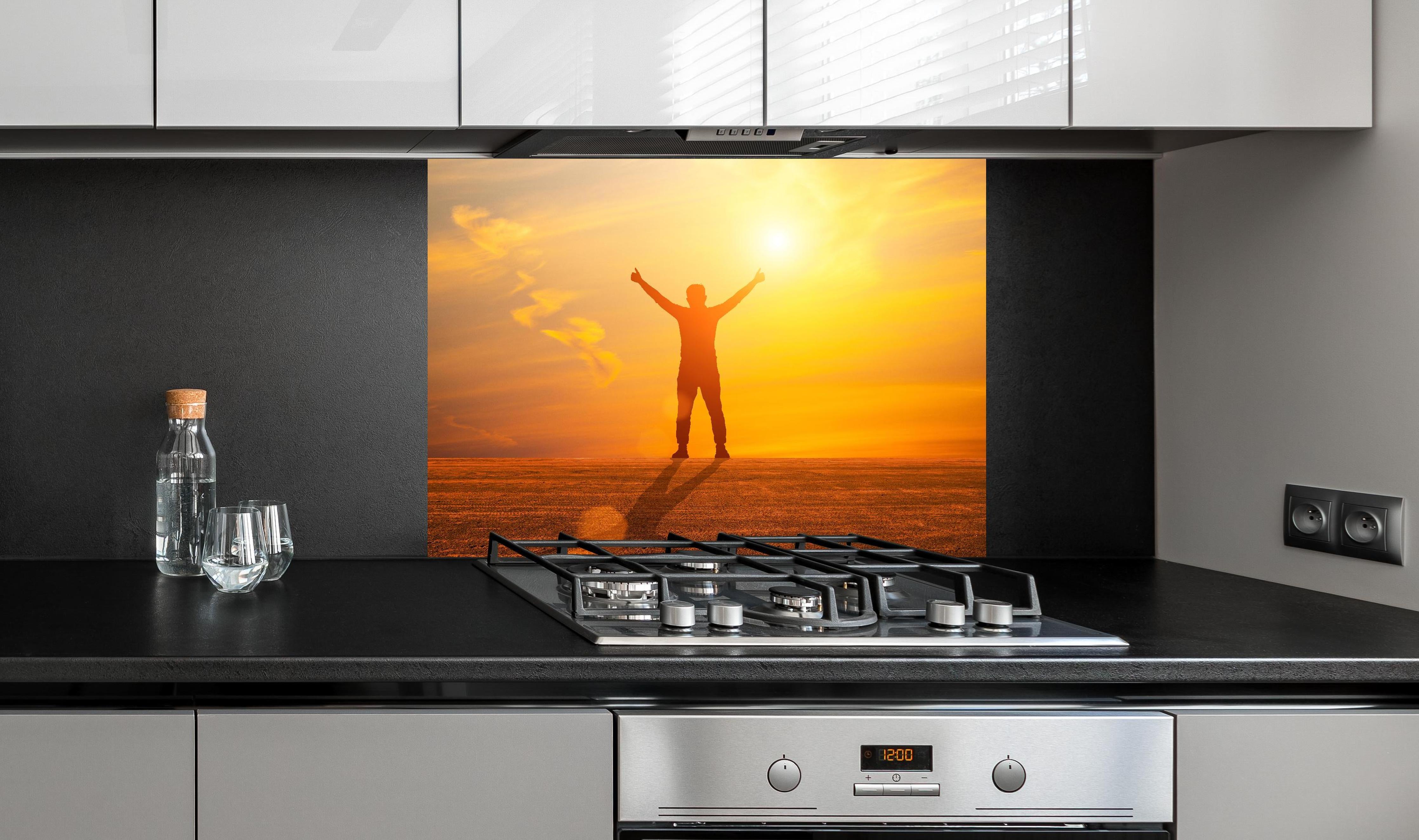 Spritzschutz - Freier Mann im goldenen Licht der Sonne hinter einem Cerankochfeld zwischen Holz-Kochutensilien