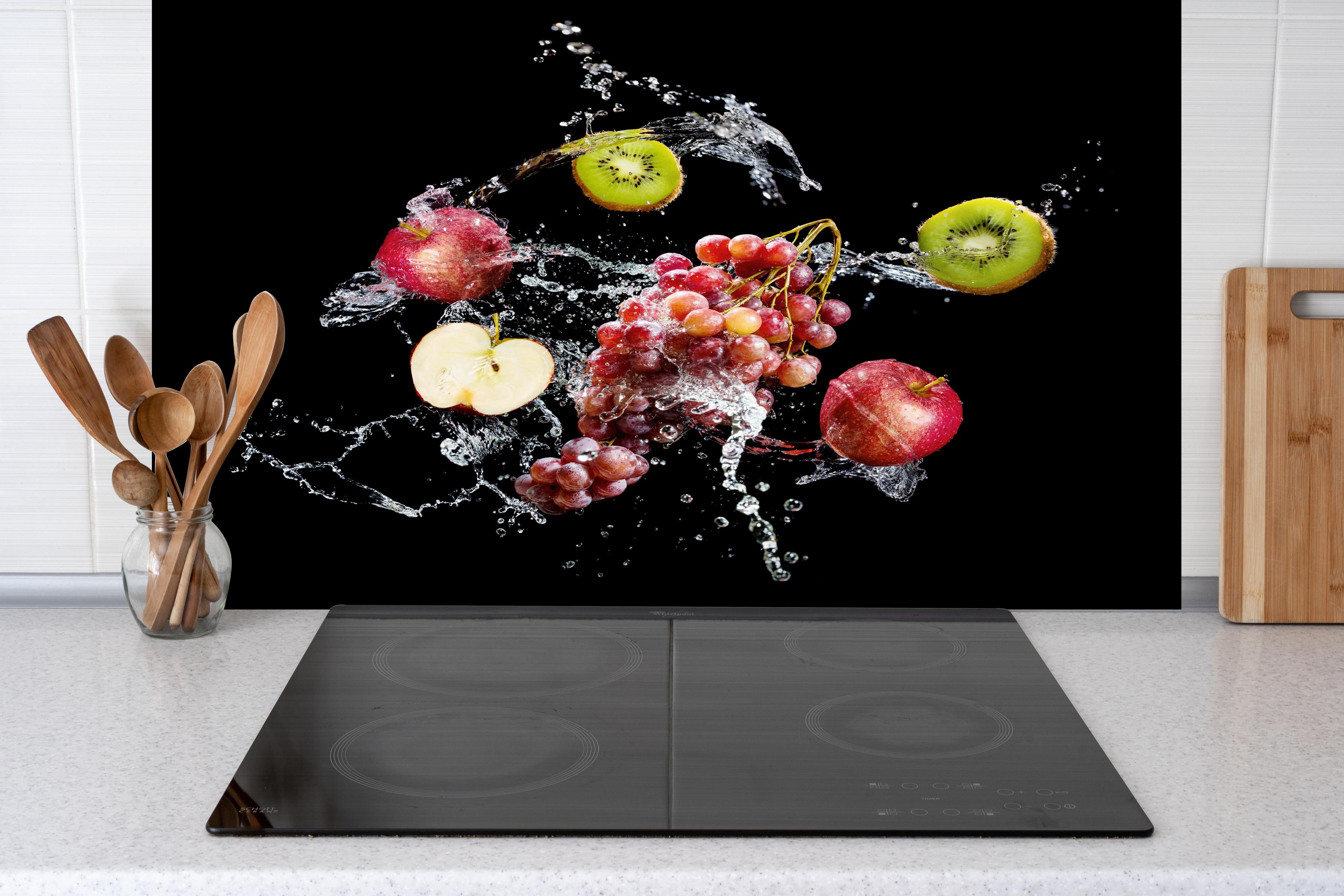 Spritzschutz - Frische Früchte im Wasser-Splash auf Schwarz hinter einem Cerankochfeld zwischen Holz-Kochutensilien