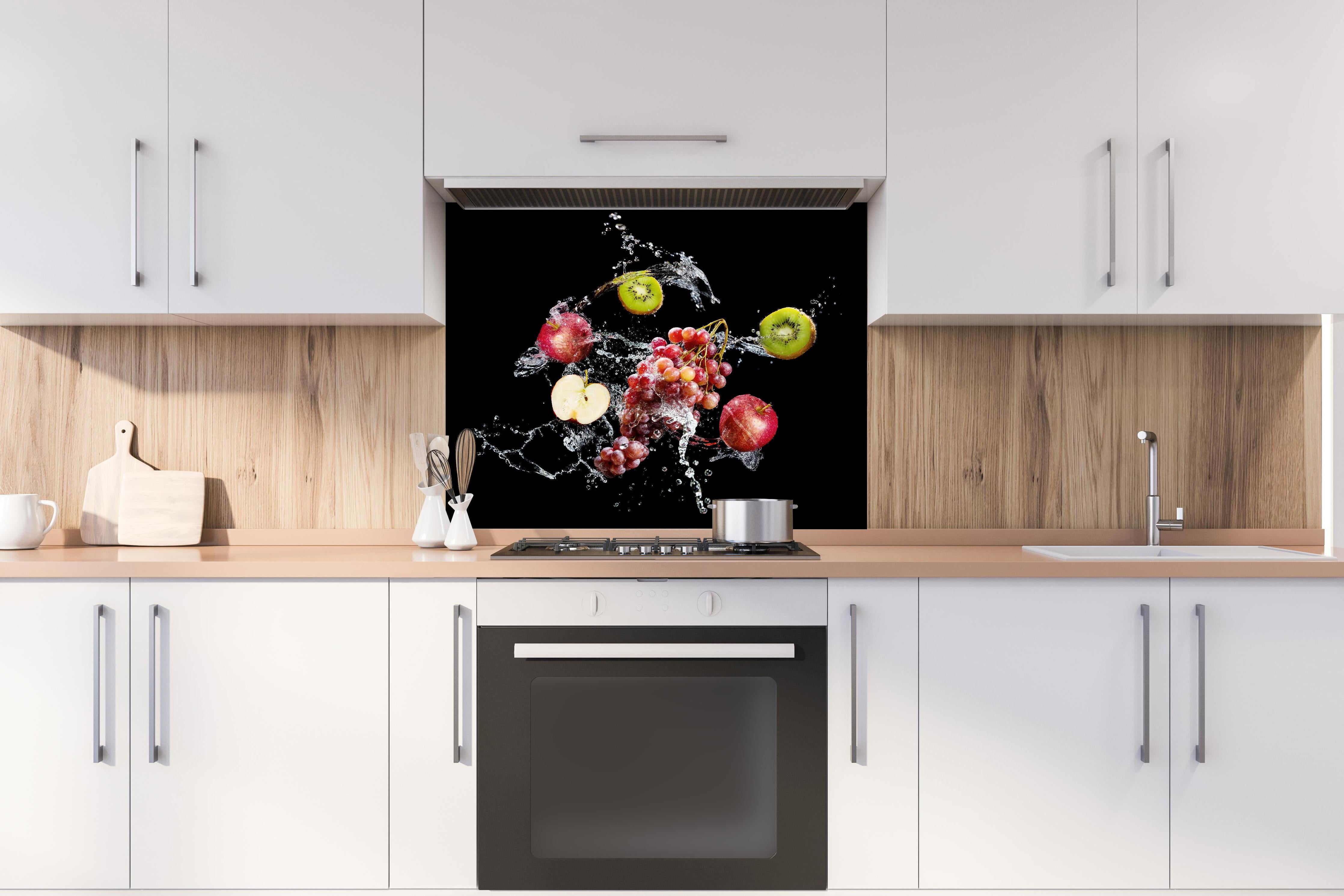 Spritzschutz - Frische Früchte im Wasser-Splash auf Schwarz hinter einem Cerankochfeld zwischen Holz-Kochutensilien