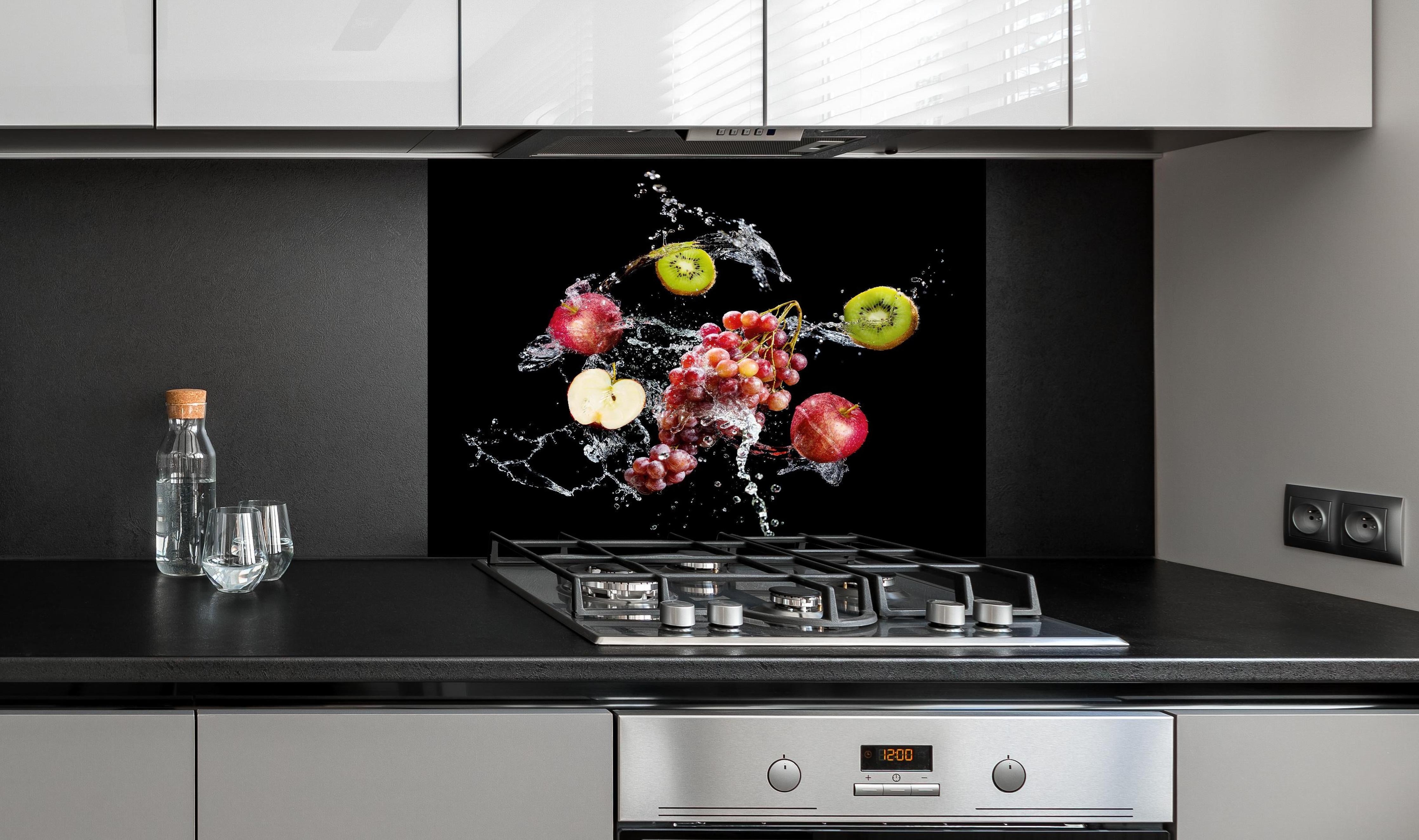 Spritzschutz - Frische Früchte im Wasser-Splash auf Schwarz hinter einem Cerankochfeld zwischen Holz-Kochutensilien