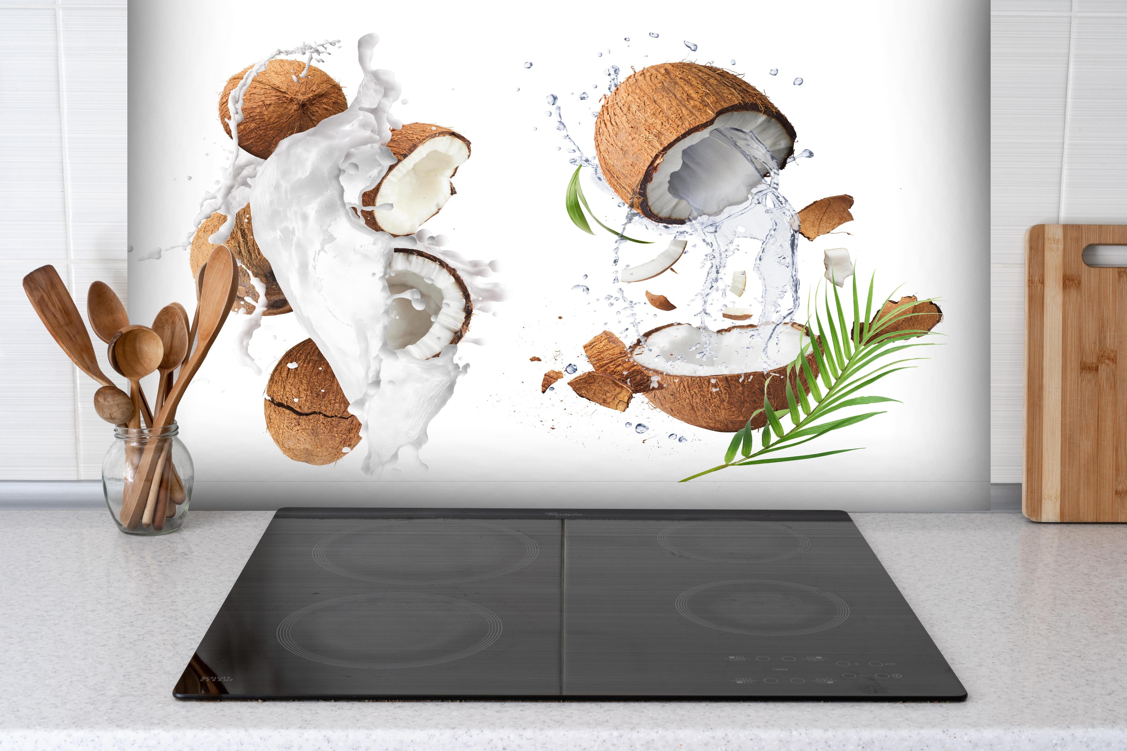 Spritzschutz - Frische Kokosnüsse hinter einem Cerankochfeld zwischen Holz-Kochutensilien