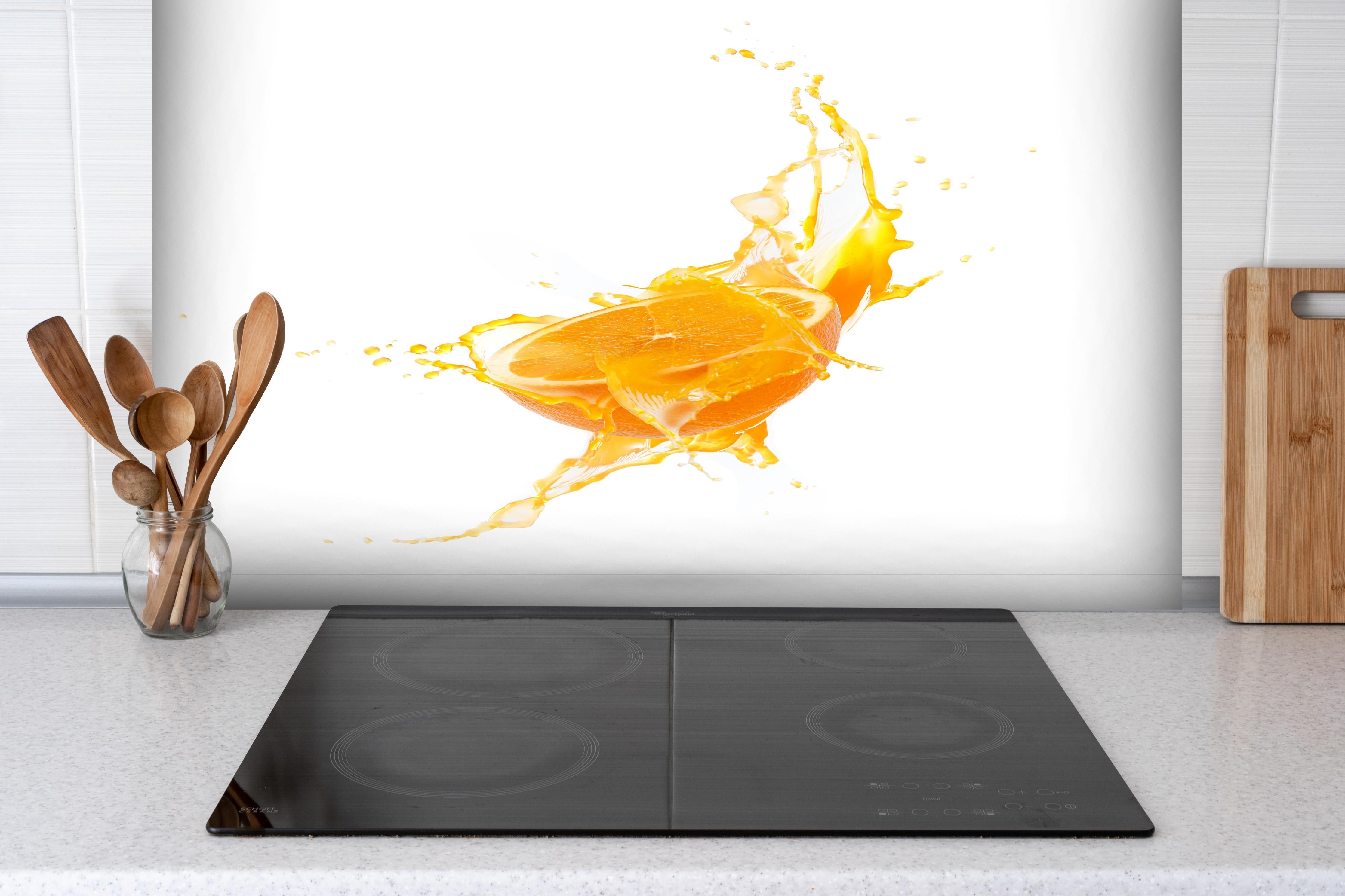 Spritzschutz - Frische Orangen-Hälfte mit Spritzwasser hinter einem Cerankochfeld zwischen Holz-Kochutensilien