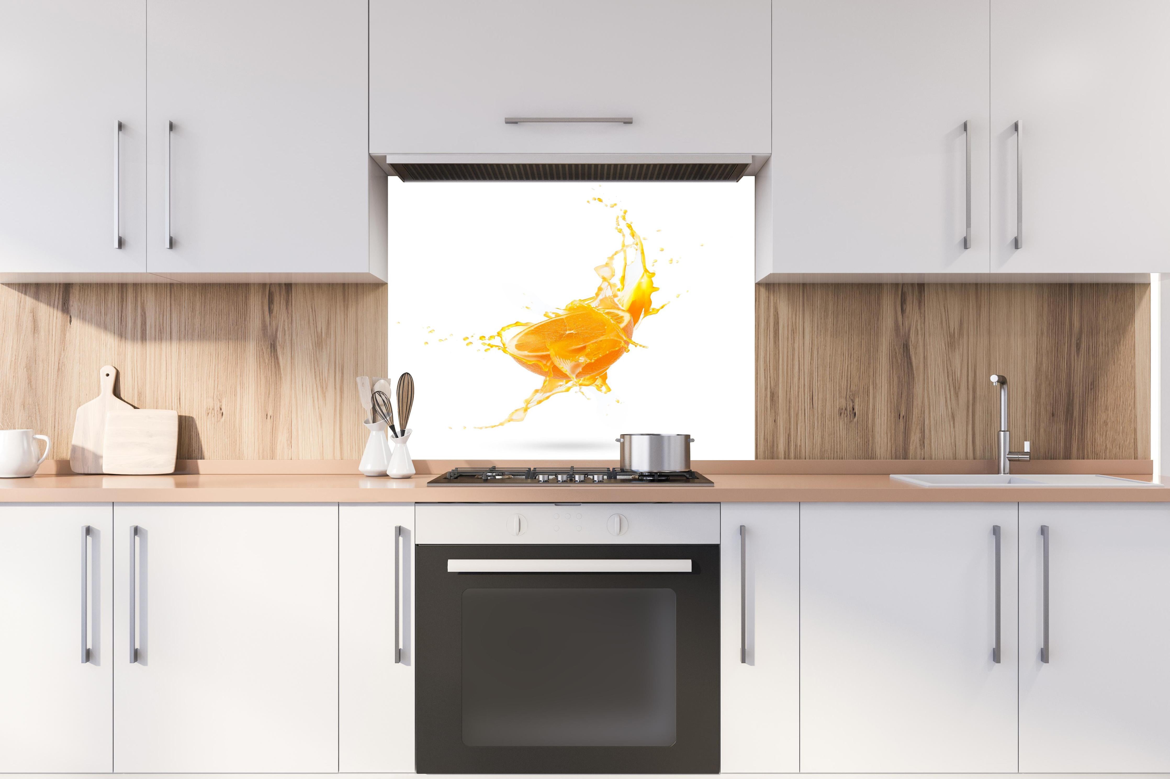 Spritzschutz - Frische Orangen-Hälfte mit Spritzwasser hinter einem Cerankochfeld zwischen Holz-Kochutensilien