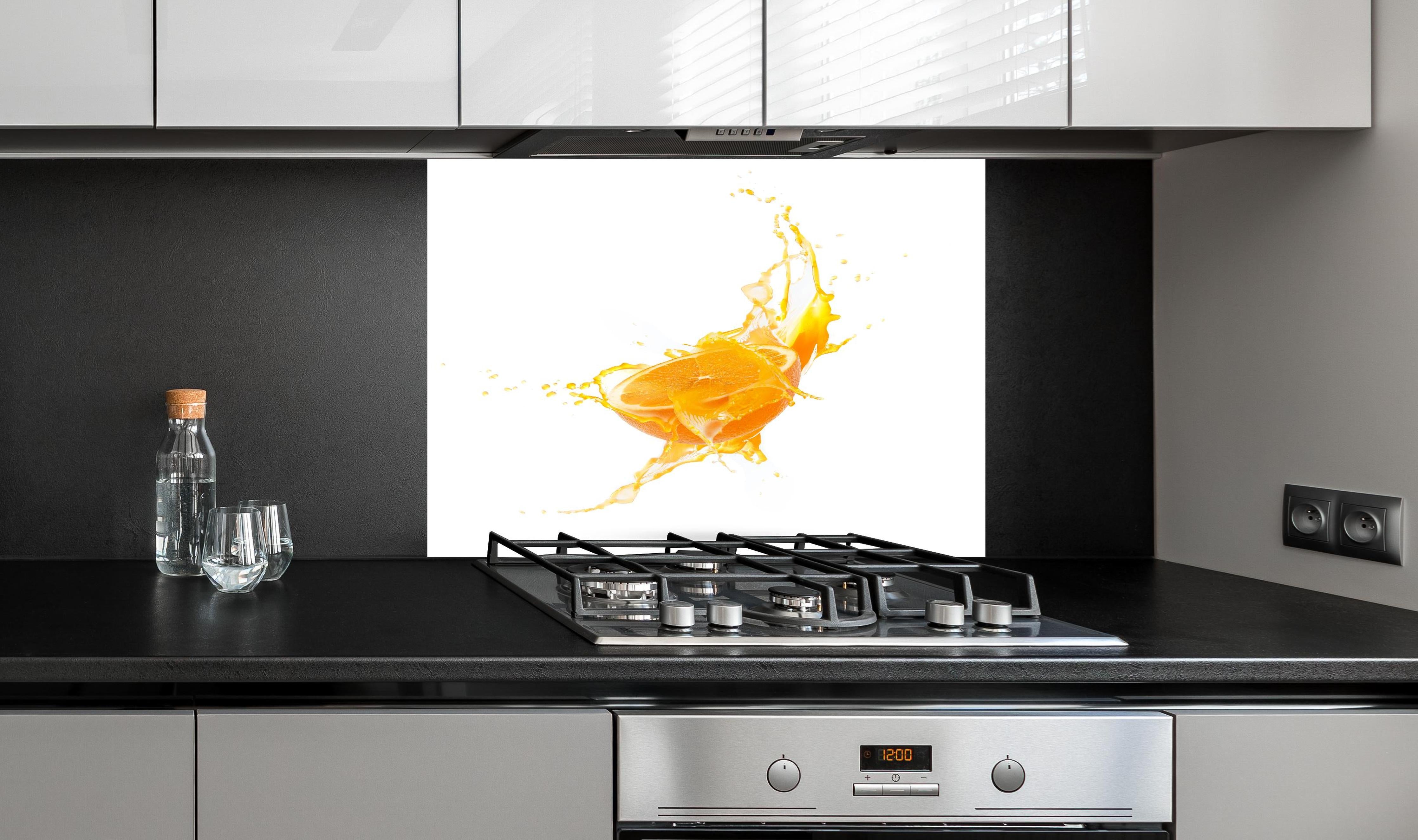 Spritzschutz - Frische Orangen-Hälfte mit Spritzwasser hinter einem Cerankochfeld zwischen Holz-Kochutensilien