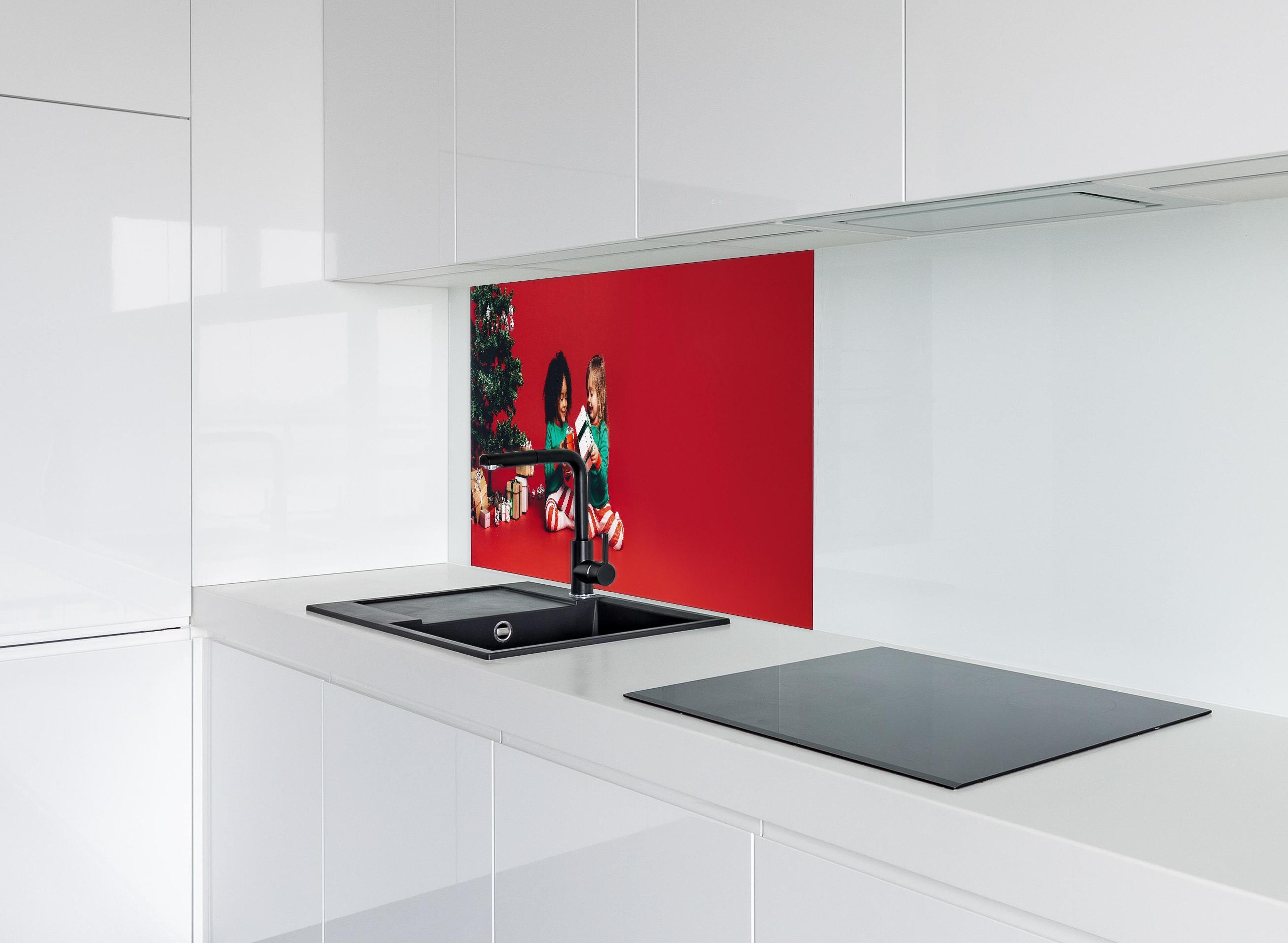 Spritzschutz - Fröhliche Kinder tauschen Weihnachtsgeschenke aus hinter einem Cerankochfeld zwischen Holz-Kochutensilien