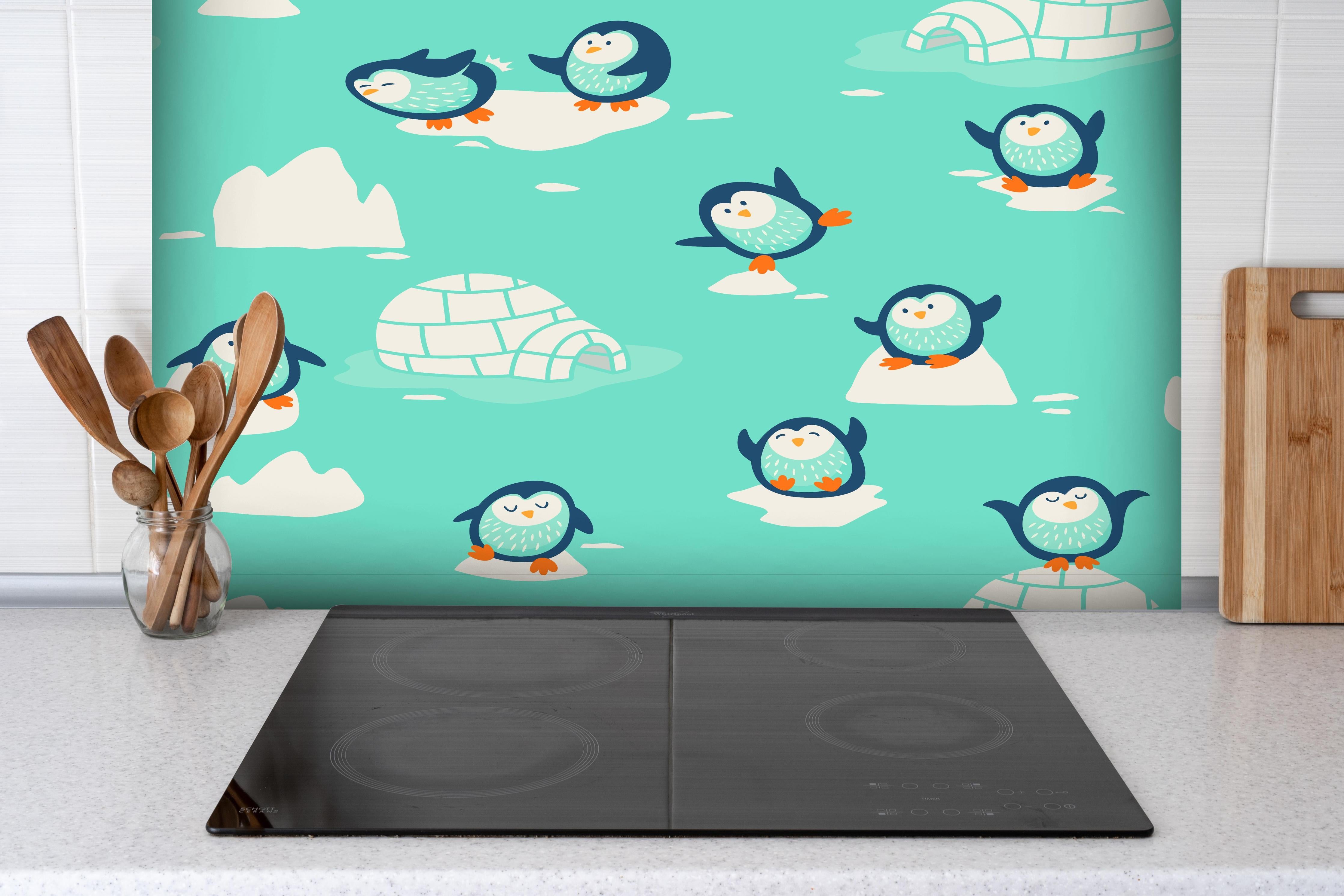 Spritzschutz - Fröhliches Pinguin-Muster auf Türkis hinter einem Cerankochfeld zwischen Holz-Kochutensilien