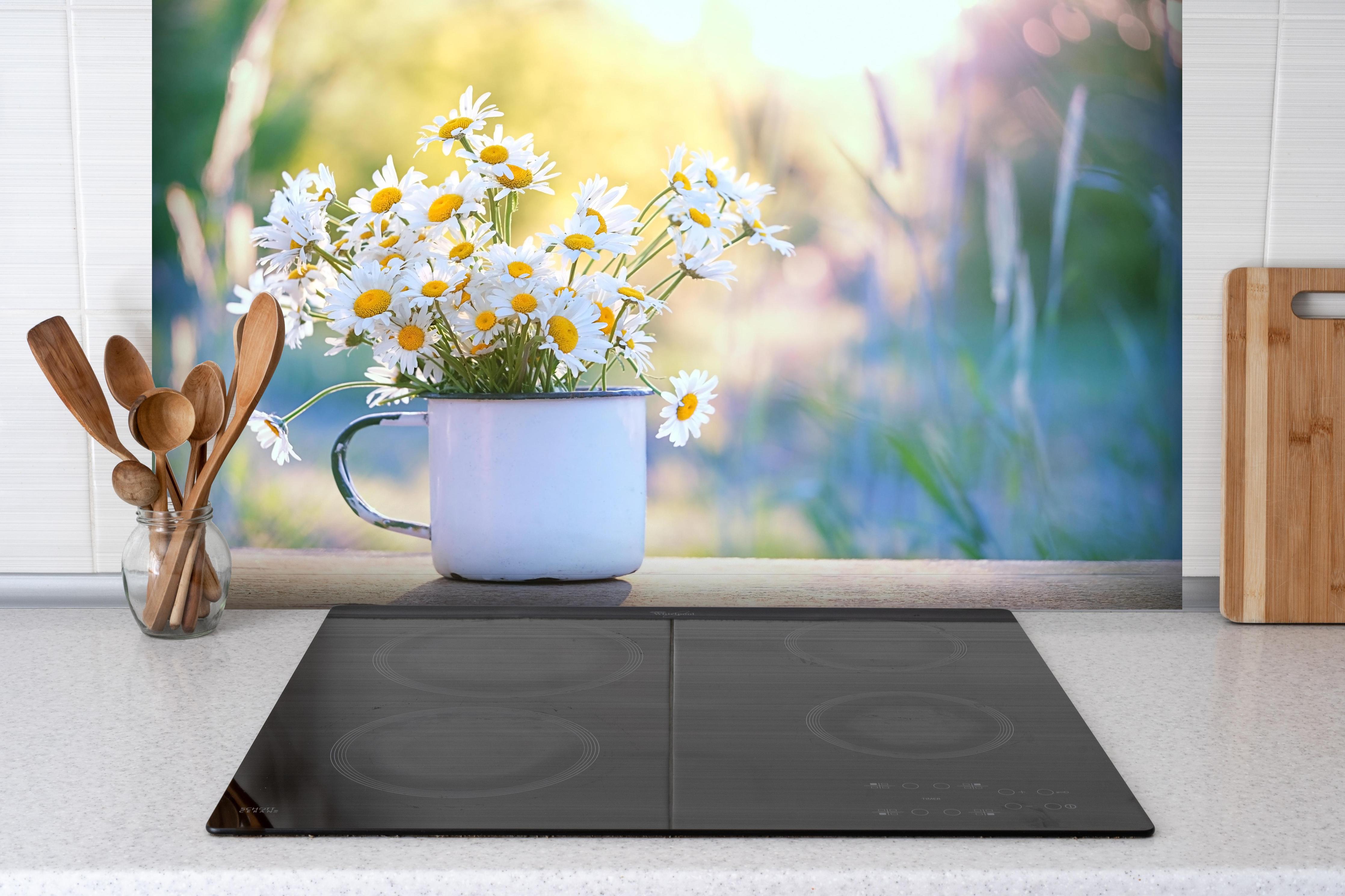 Spritzschutz - Gänseblümchen im Licht des Sonnenuntergangs hinter einem Cerankochfeld zwischen Holz-Kochutensilien