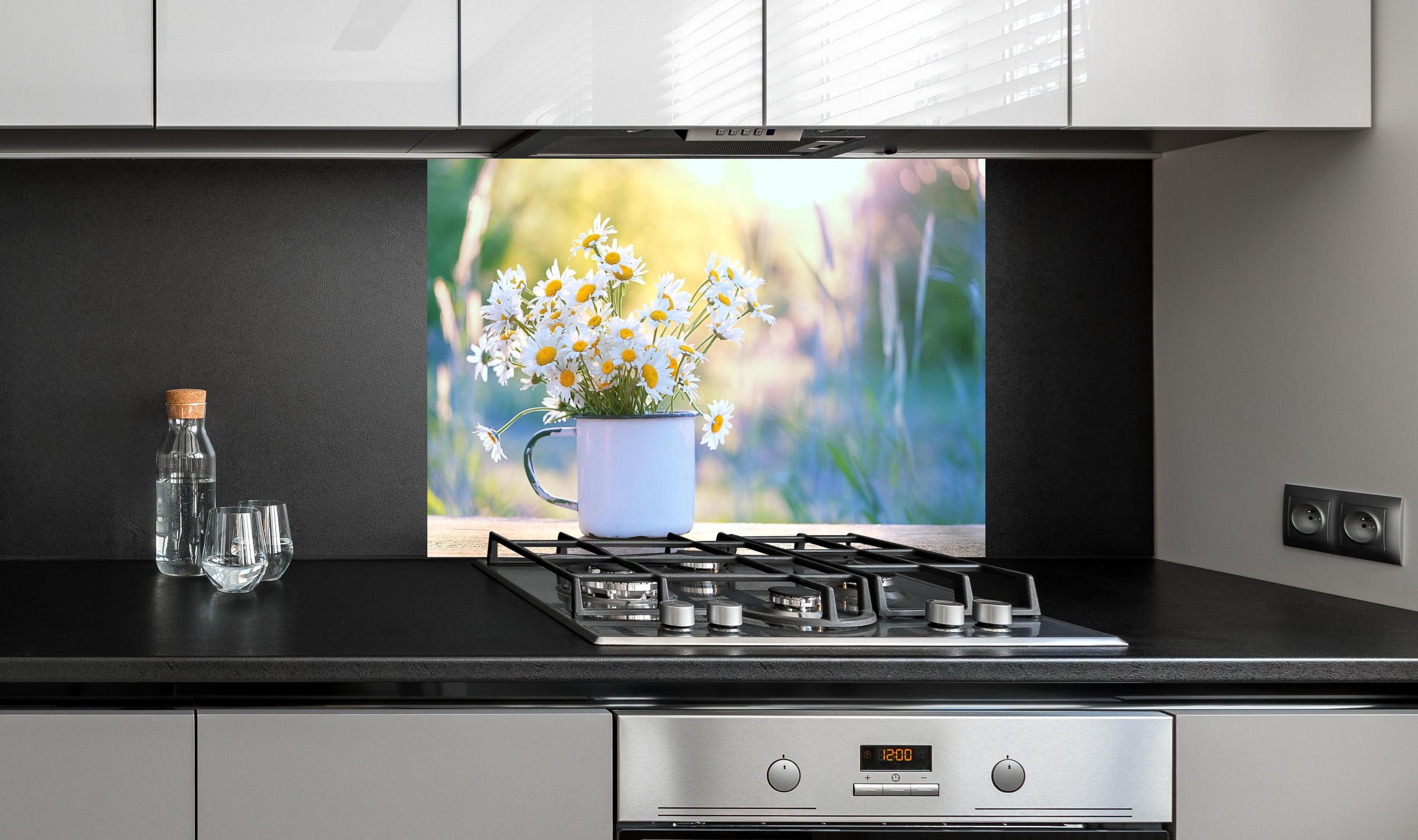 Spritzschutz - Gänseblümchen im Licht des Sonnenuntergangs hinter einem Cerankochfeld zwischen Holz-Kochutensilien