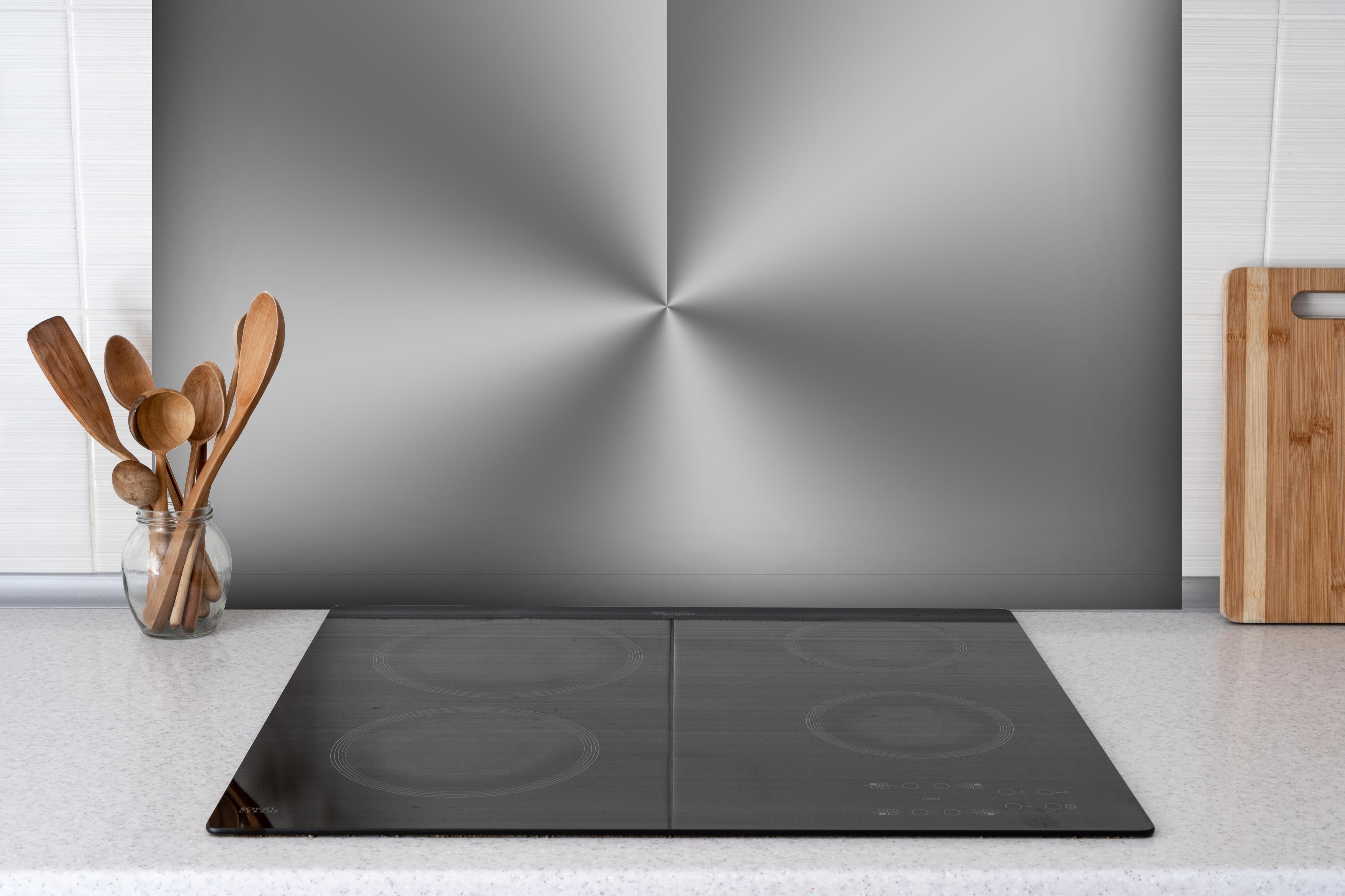 Spritzschutz - Gebürstetes Metall hinter einem Cerankochfeld zwischen Holz-Kochutensilien