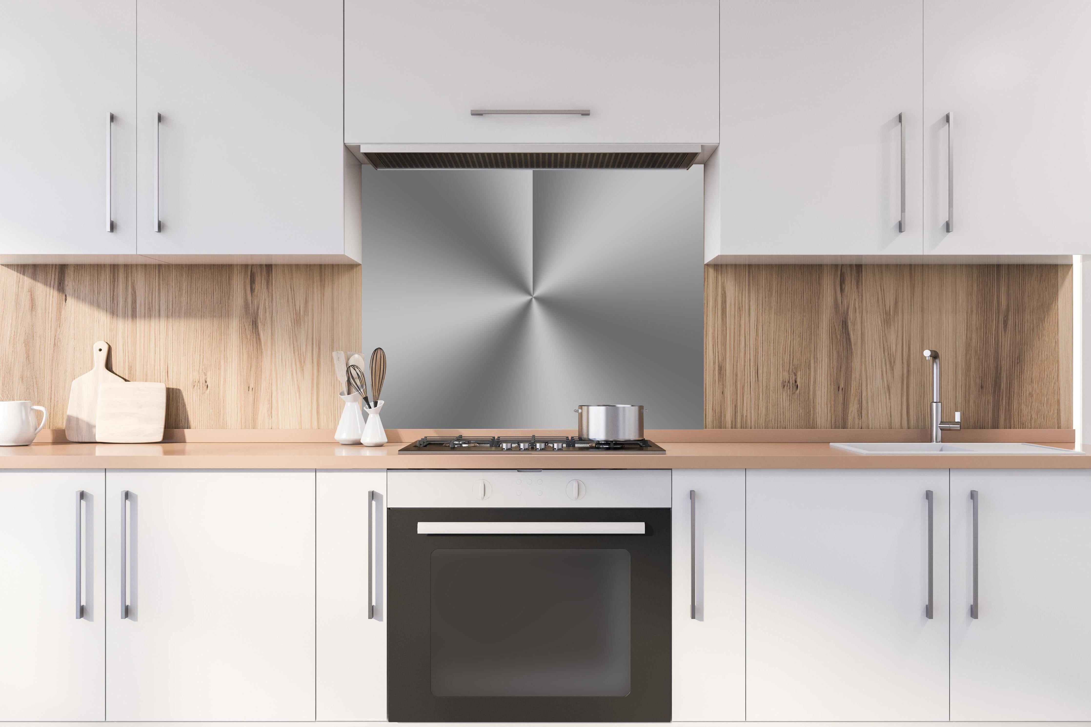 Spritzschutz - Gebürstetes Metall hinter einem Cerankochfeld zwischen Holz-Kochutensilien