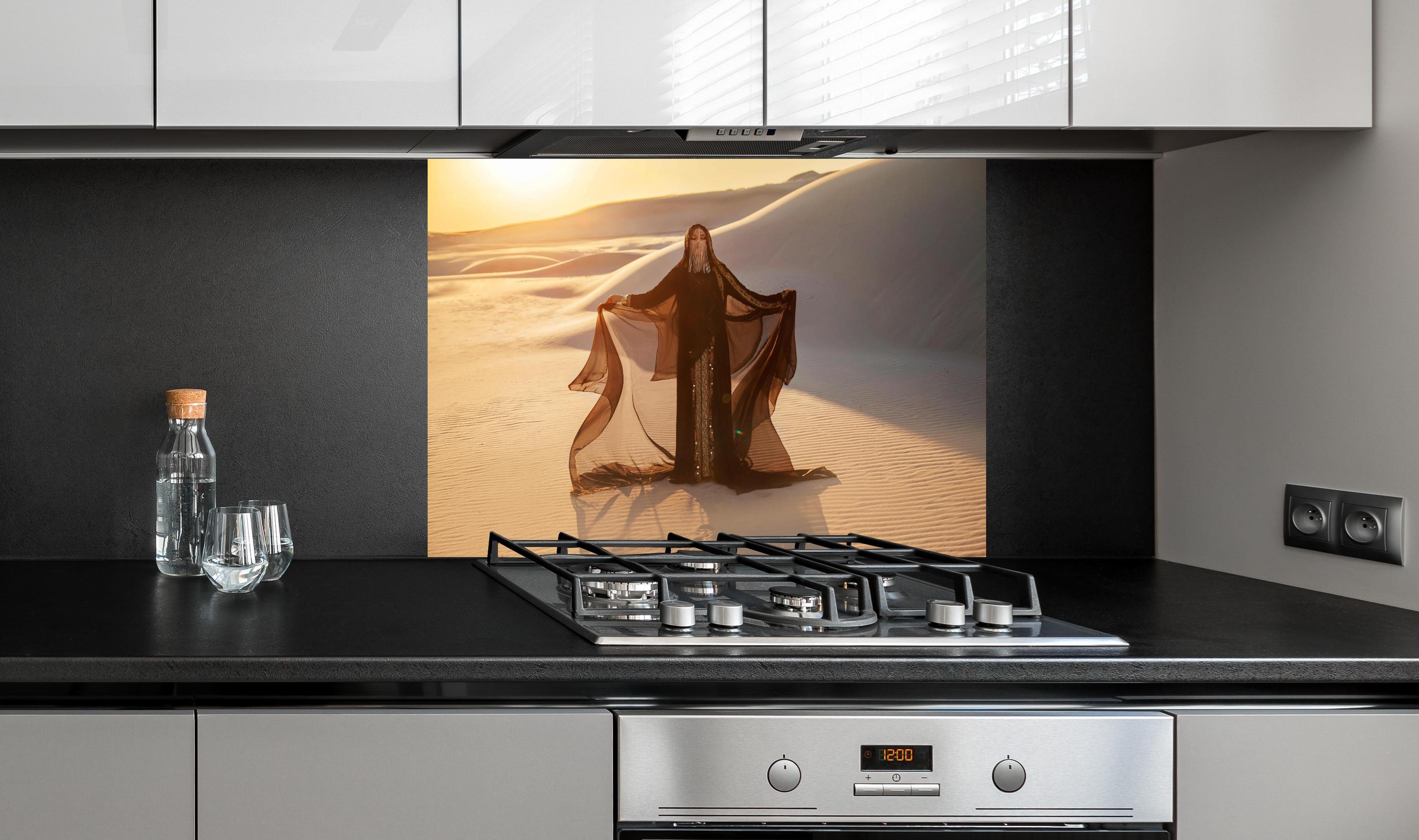 Spritzschutz - Geheimnisvolle Frau steht in arabischer Savanne hinter einem Cerankochfeld zwischen Holz-Kochutensilien