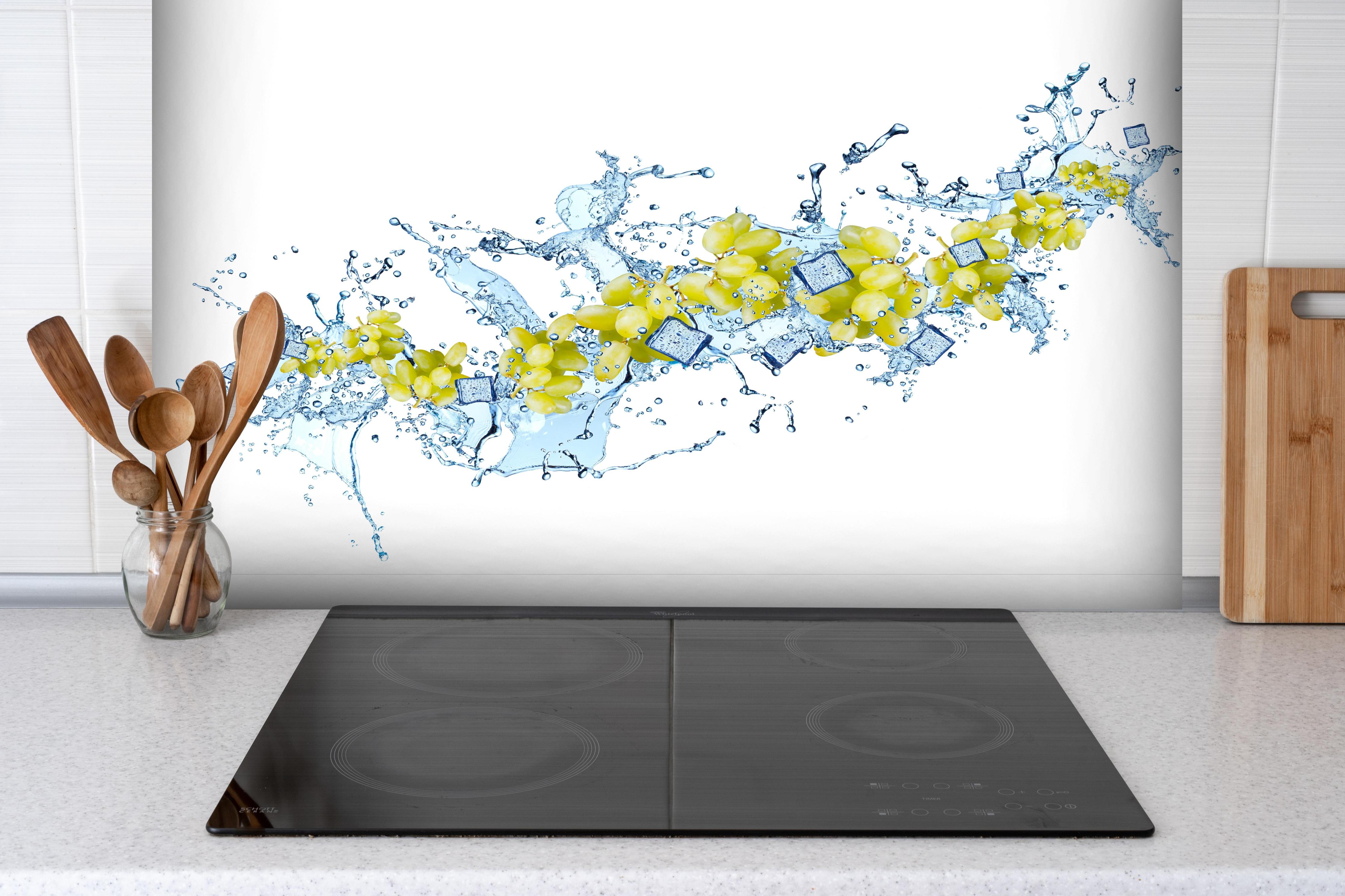 Spritzschutz - Gelbe Trauben mit dynamischem Wasser Splash hinter einem Cerankochfeld zwischen Holz-Kochutensilien