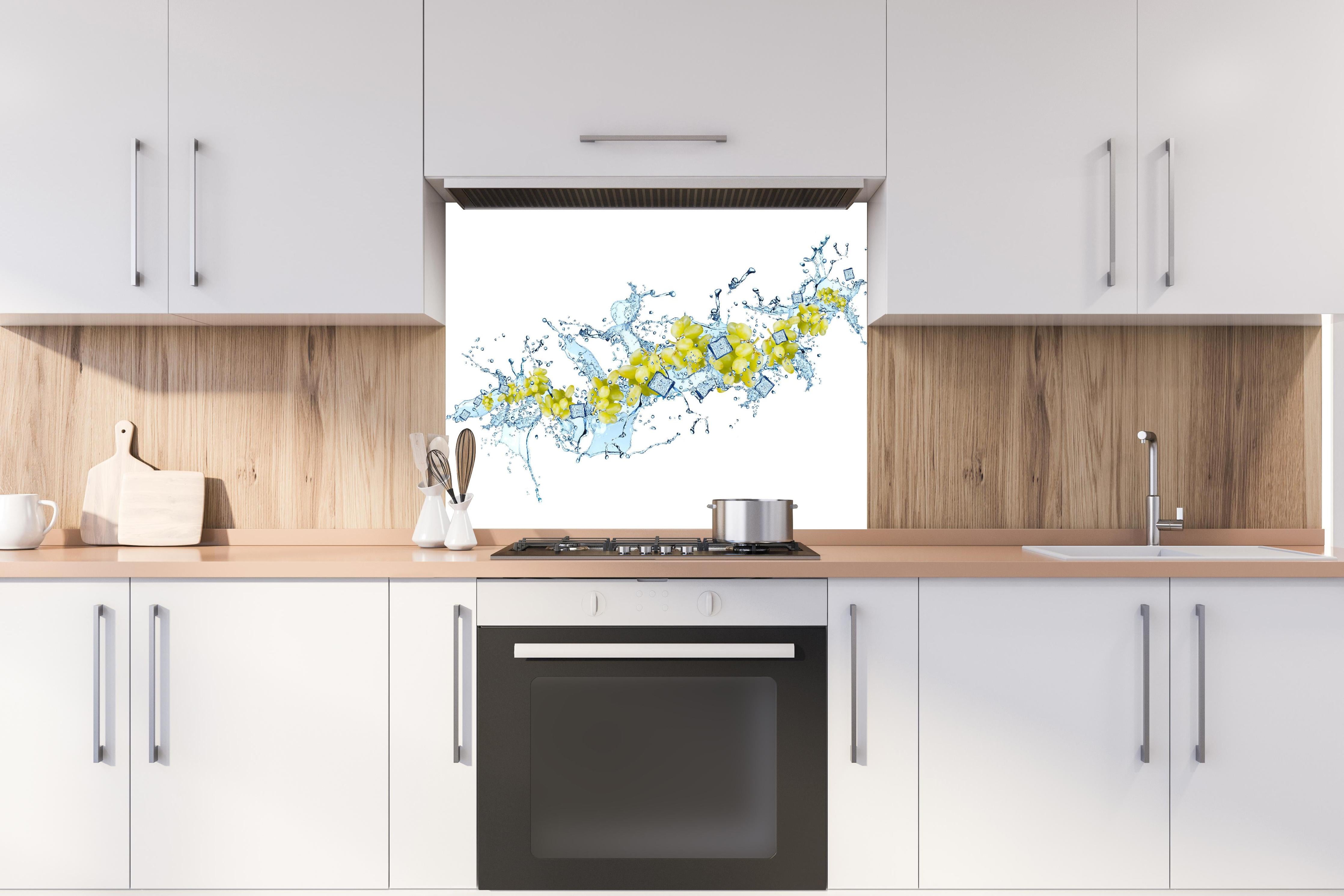 Spritzschutz - Gelbe Trauben mit dynamischem Wasser Splash hinter einem Cerankochfeld zwischen Holz-Kochutensilien