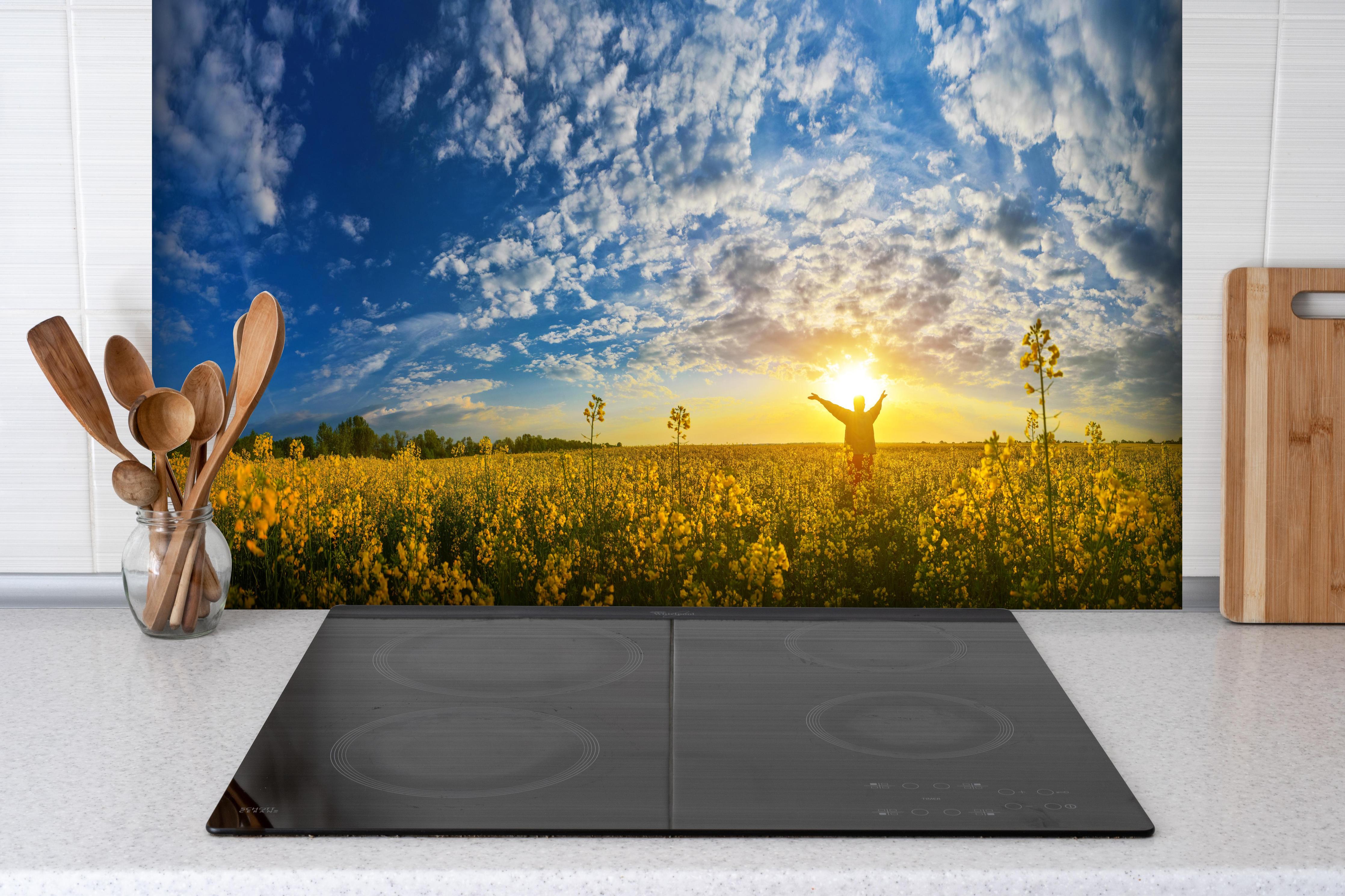 Spritzschutz - Gelbliches Blumenfeld am Morgen hinter einem Cerankochfeld zwischen Holz-Kochutensilien