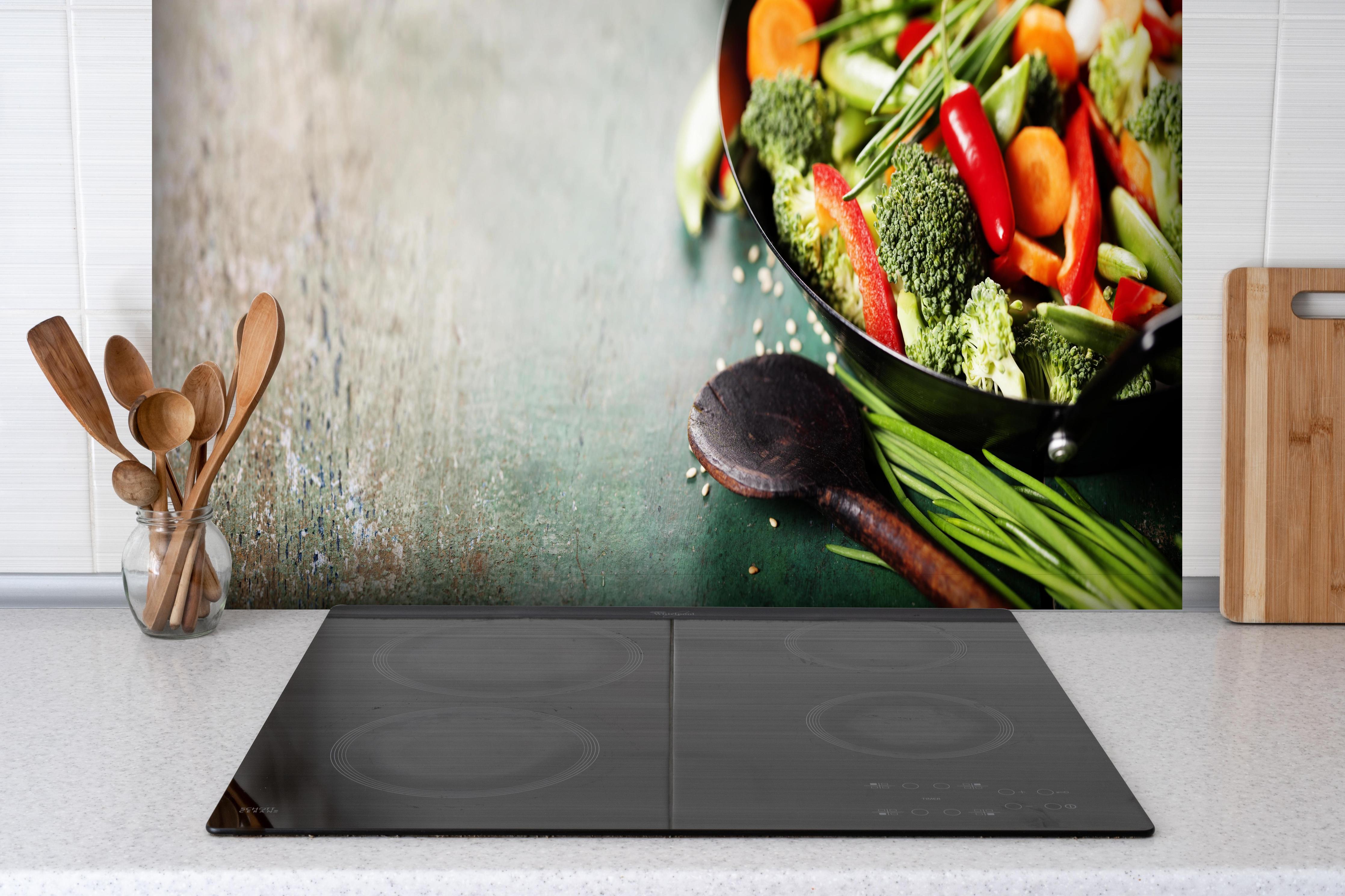 Spritzschutz - Gemüse kochen im Wok hinter einem Cerankochfeld zwischen Holz-Kochutensilien