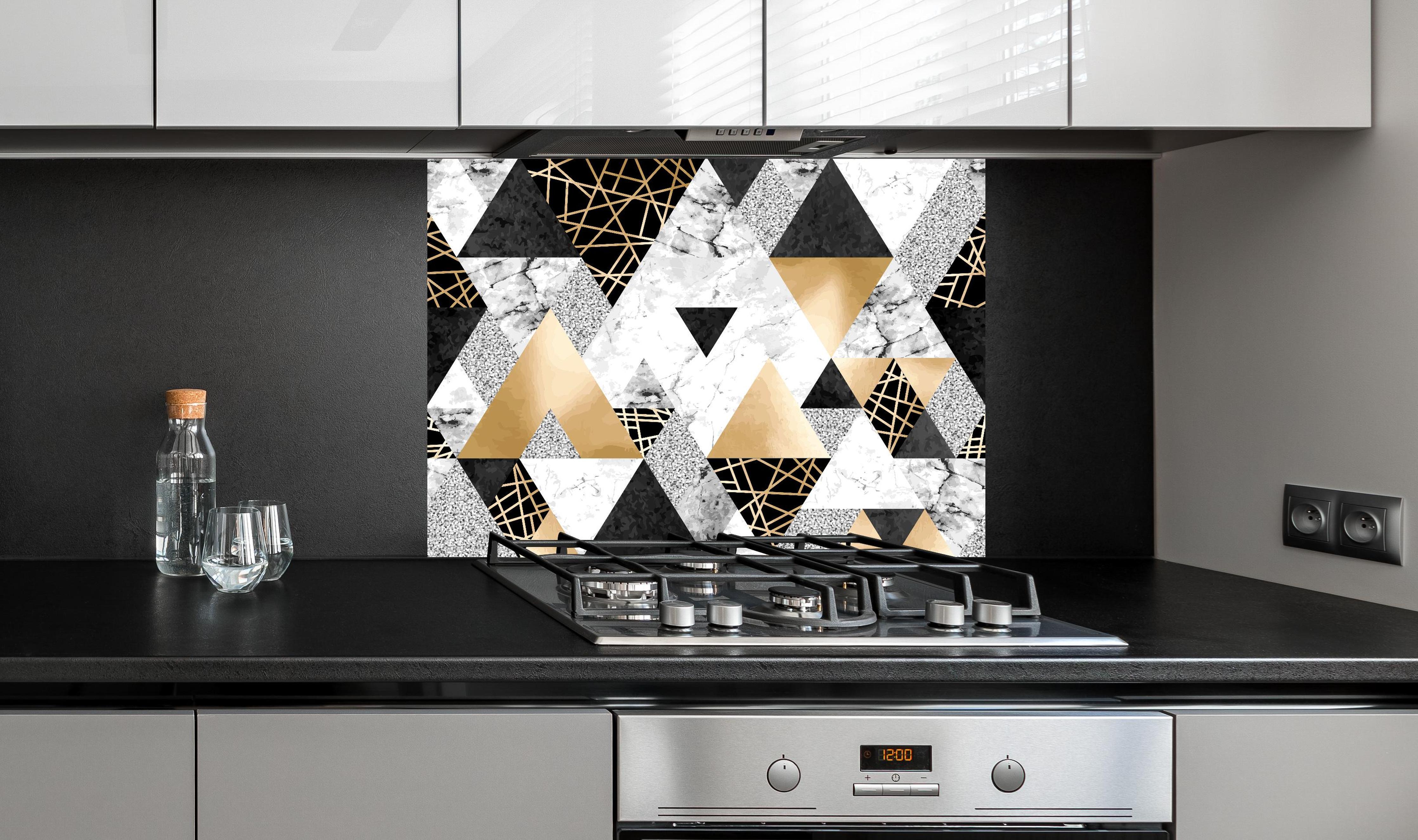 Spritzschutz - Geometrisches Muster in Gold, Schwarz und Weiß hinter einem Cerankochfeld zwischen Holz-Kochutensilien
