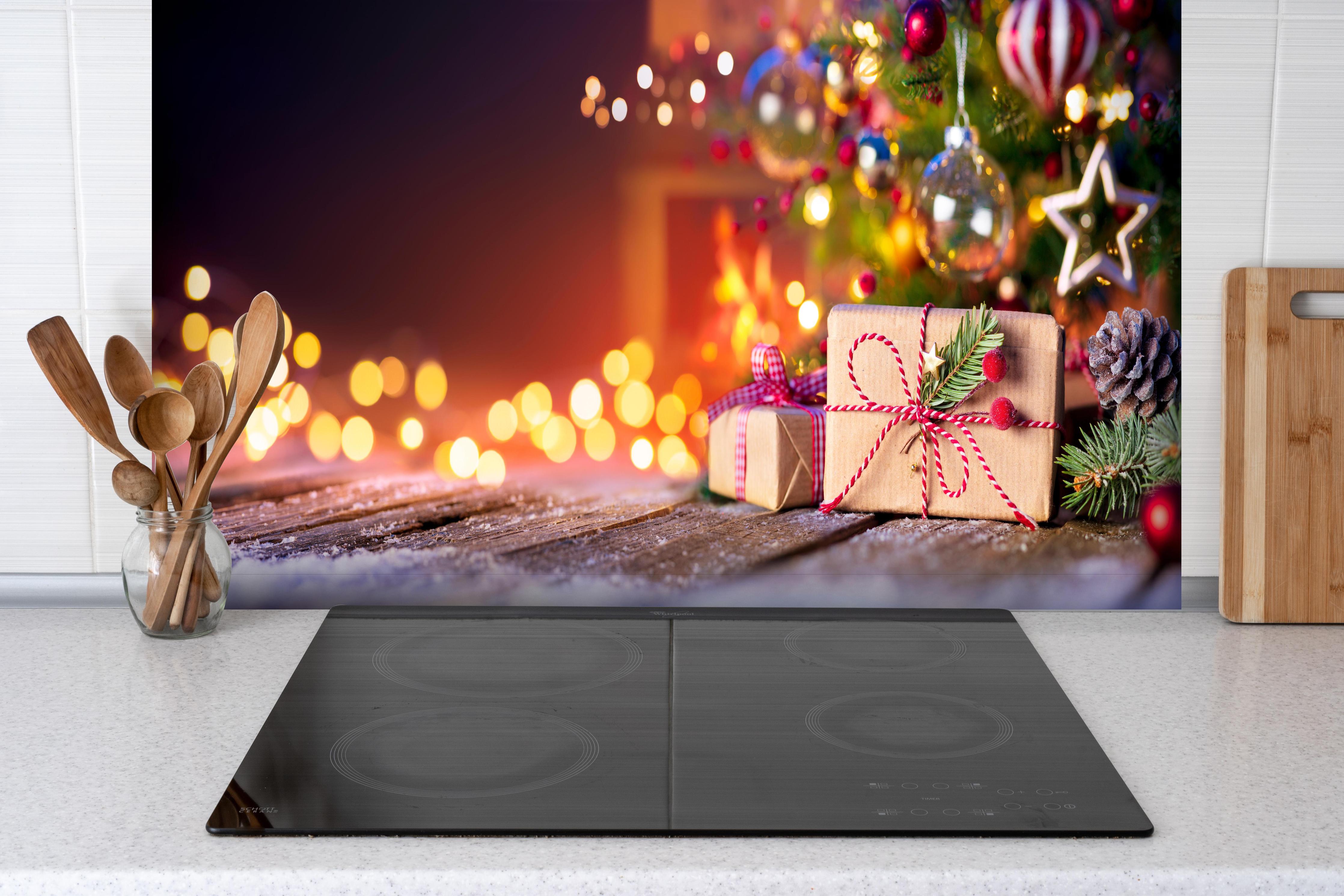 Spritzschutz - Geschenke unter dem Weihnachtsbaum hinter einem Cerankochfeld zwischen Holz-Kochutensilien