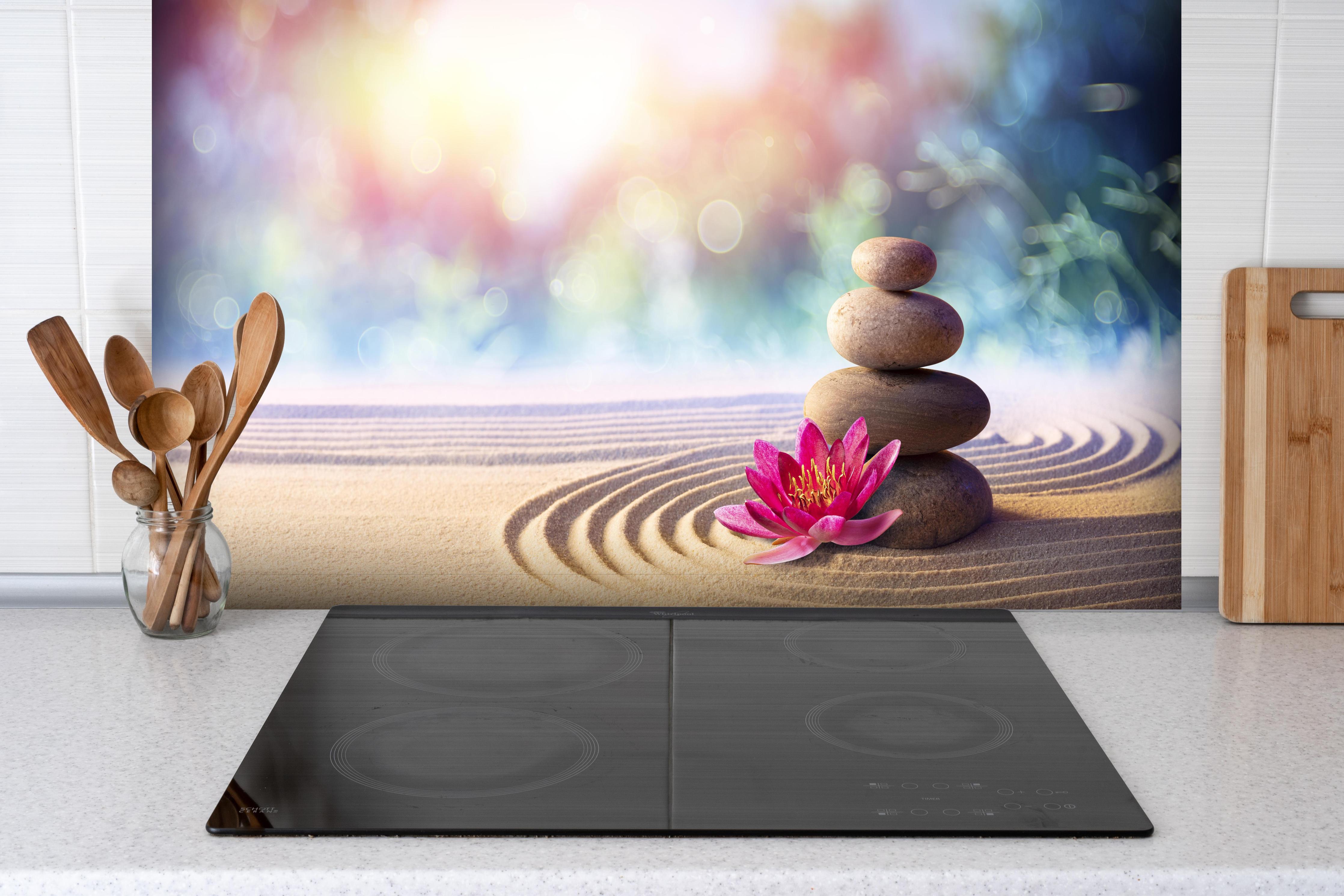 Spritzschutz - Gestapelte Meditation Steine hinter einem Cerankochfeld zwischen Holz-Kochutensilien