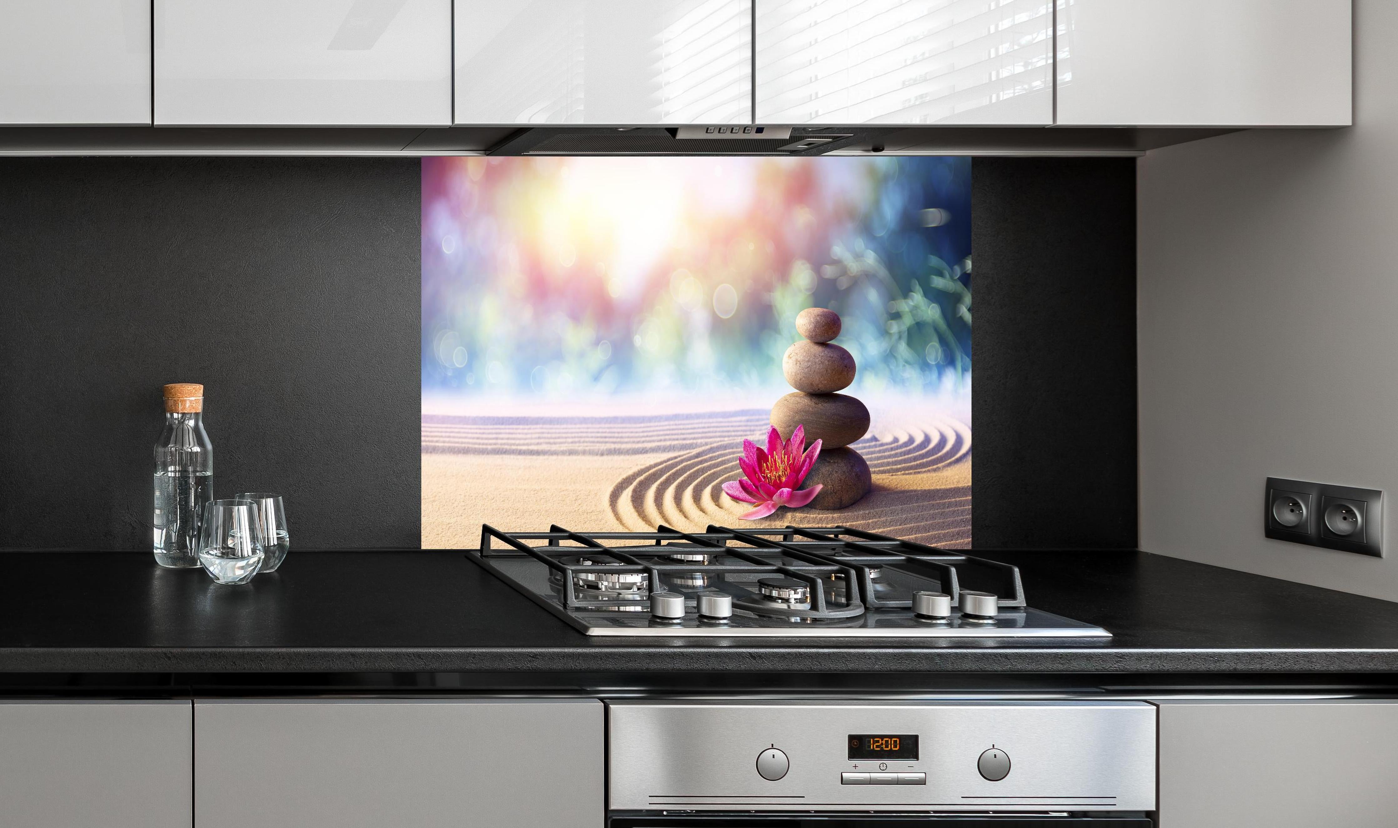 Spritzschutz - Gestapelte Meditation Steine hinter einem Cerankochfeld zwischen Holz-Kochutensilien