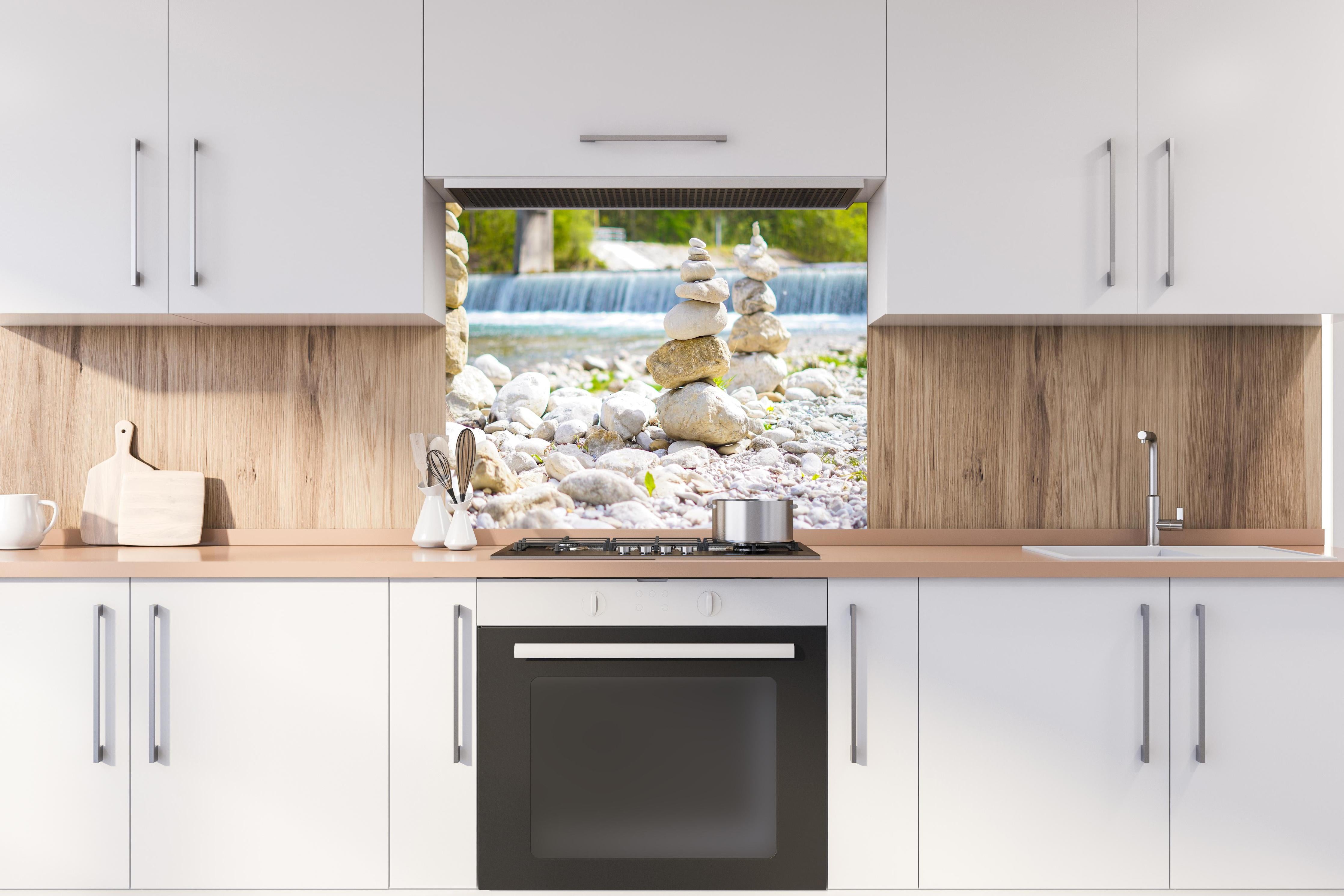 Spritzschutz - Gestapelte Steine am Fluss in Weiß-Grau hinter einem Cerankochfeld zwischen Holz-Kochutensilien