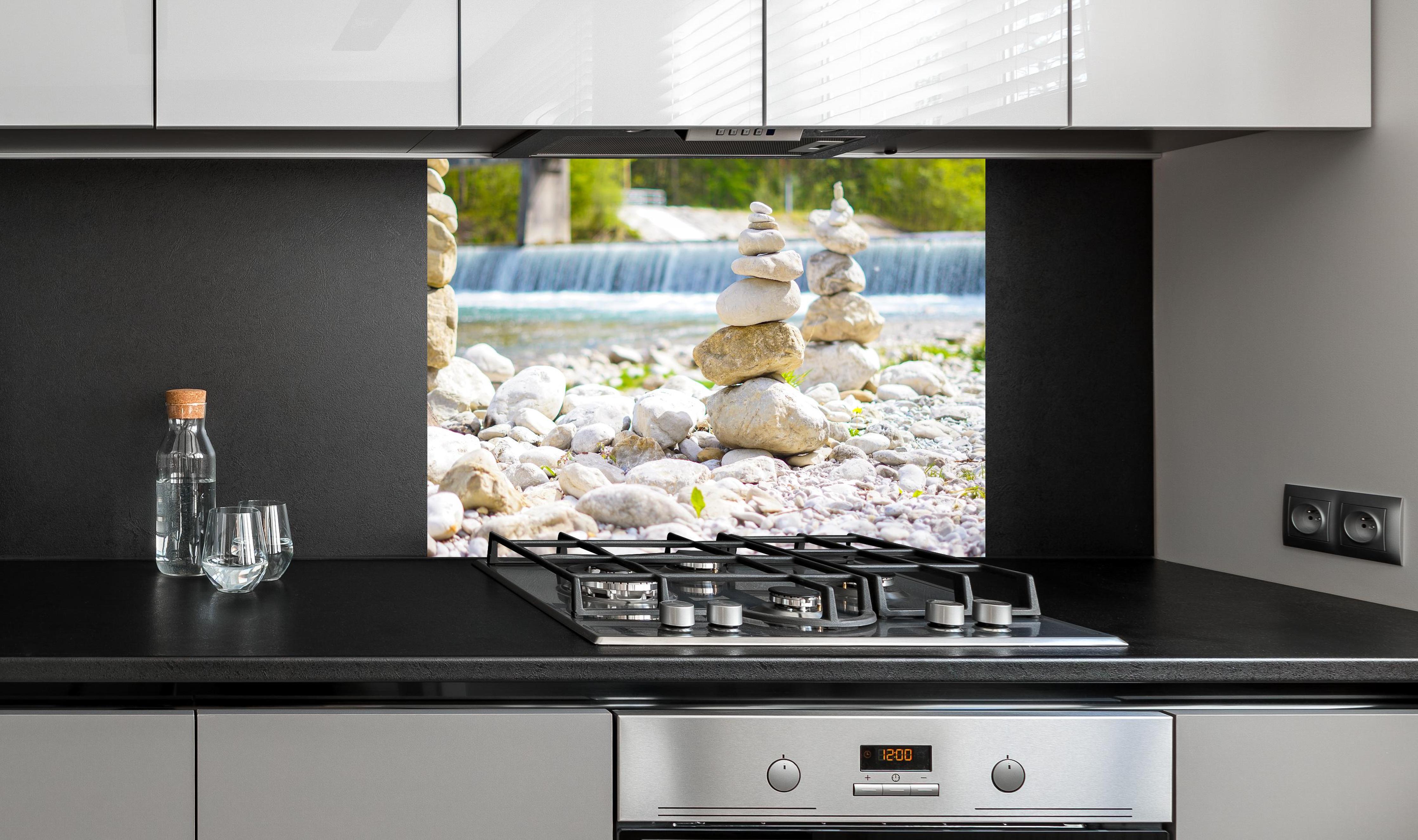 Spritzschutz - Gestapelte Steine am Fluss in Weiß-Grau hinter einem Cerankochfeld zwischen Holz-Kochutensilien