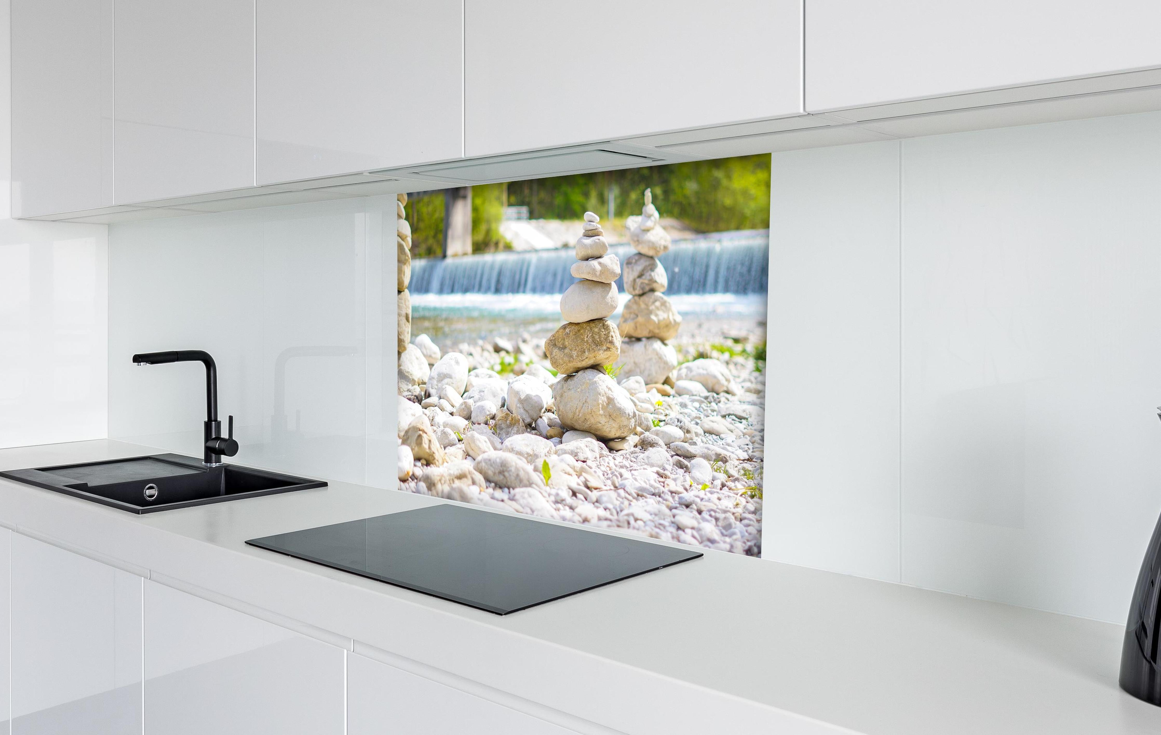 Spritzschutz - Gestapelte Steine am Fluss in Weiß-Grau hinter einem Cerankochfeld zwischen Holz-Kochutensilien