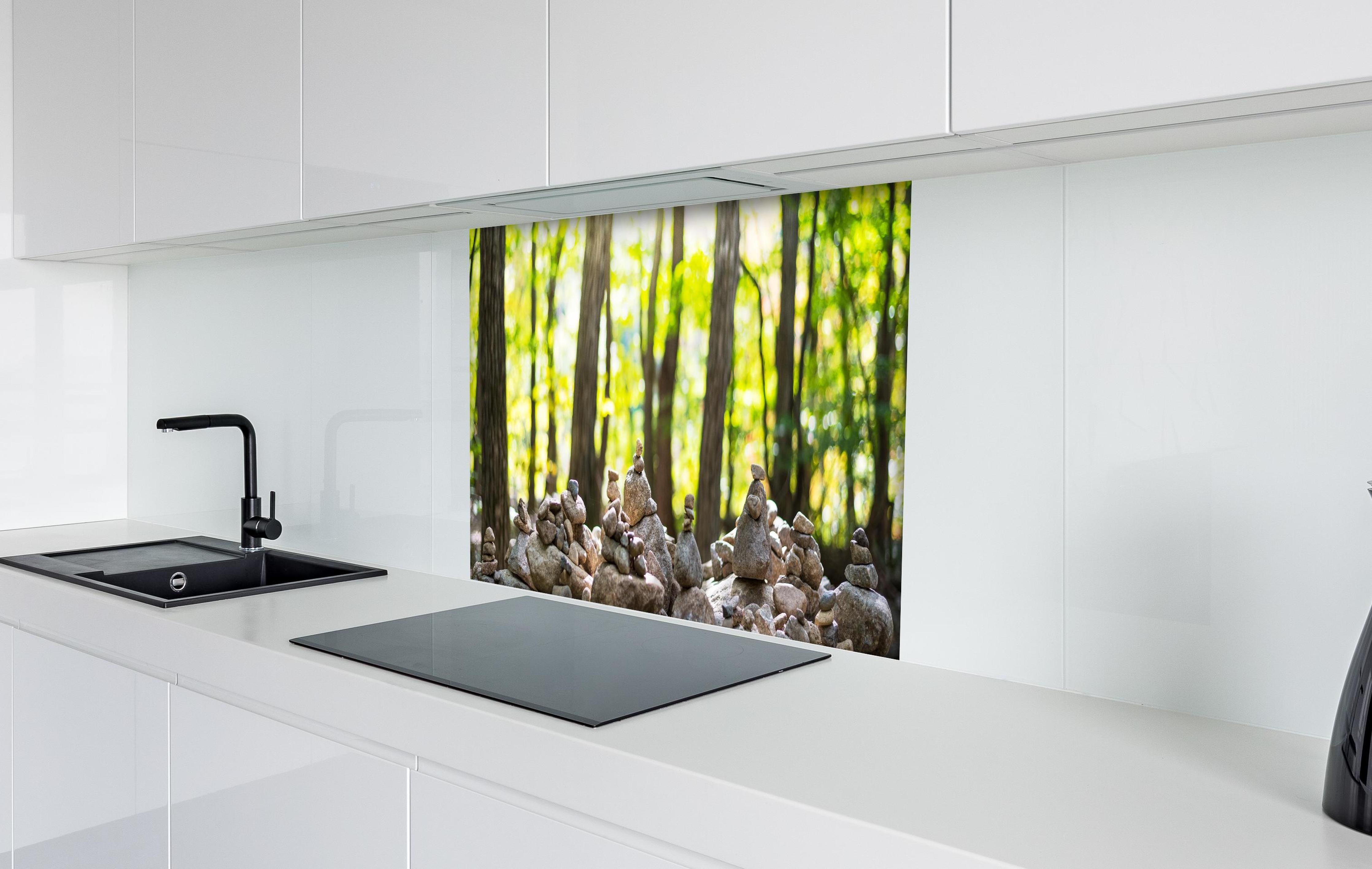 Spritzschutz - Gestapelte Steine mit Waldhintergrund hinter einem Cerankochfeld zwischen Holz-Kochutensilien