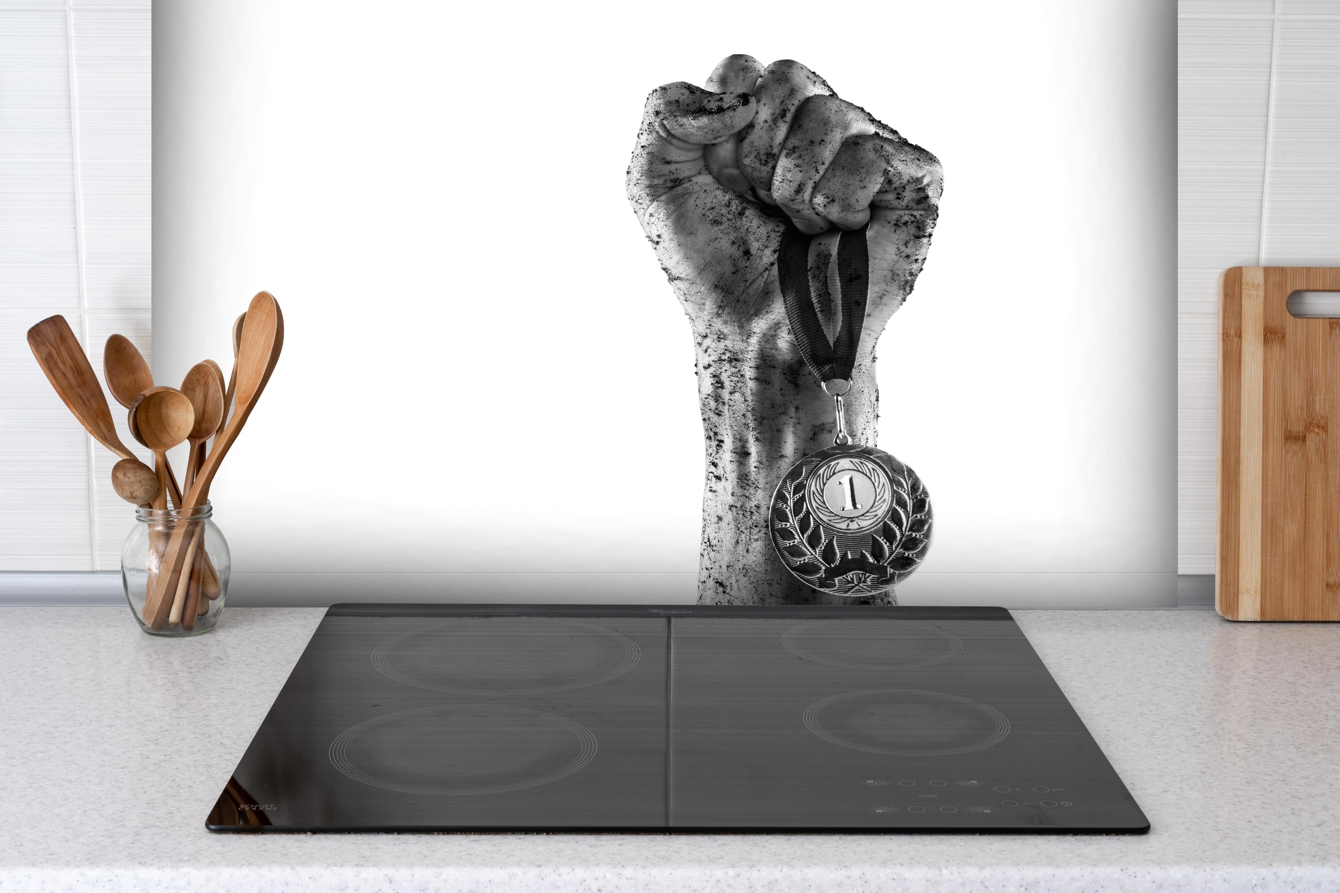 Spritzschutz - Gewinner mit einer Medaille hinter einem Cerankochfeld zwischen Holz-Kochutensilien