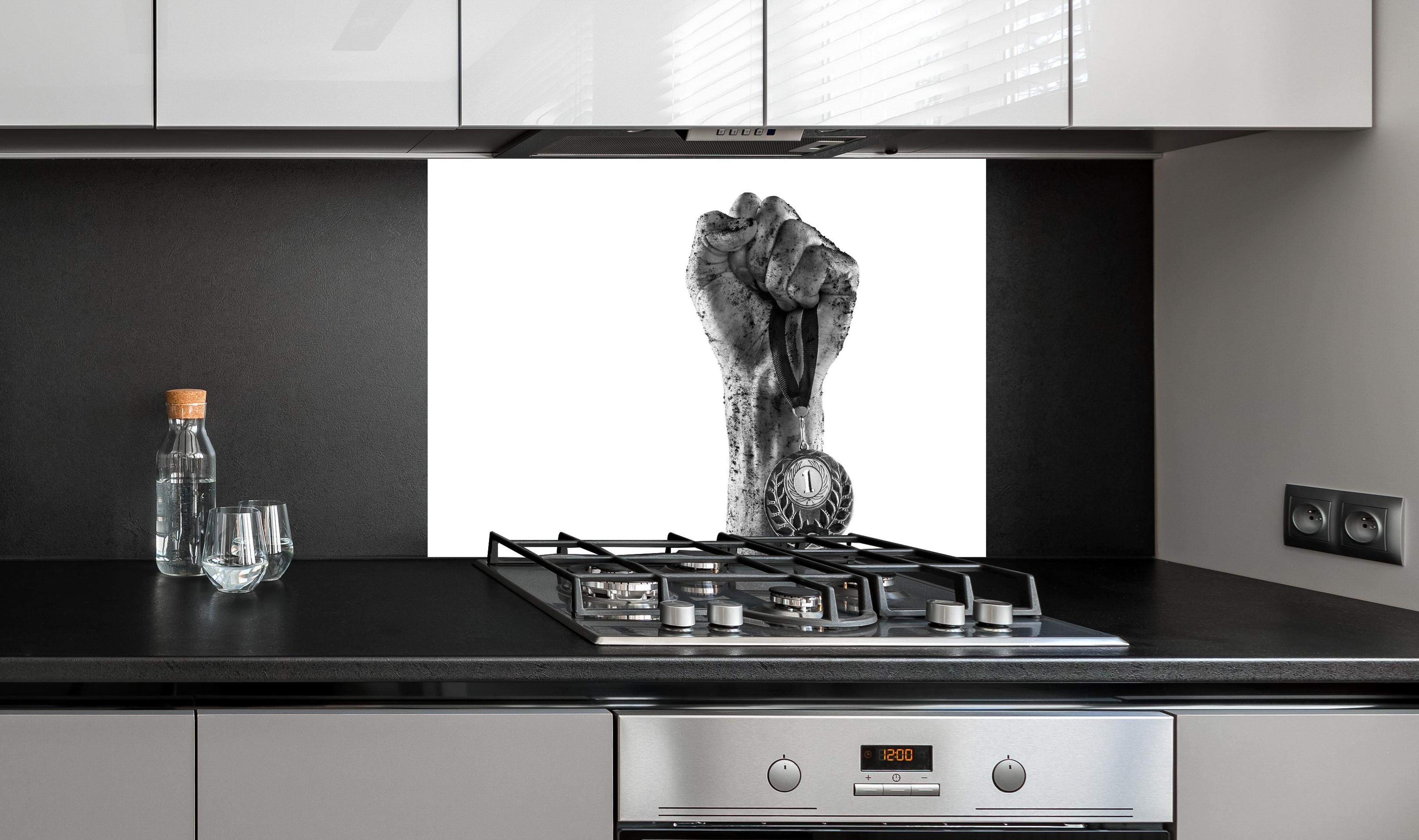 Spritzschutz - Gewinner mit einer Medaille hinter einem Cerankochfeld zwischen Holz-Kochutensilien