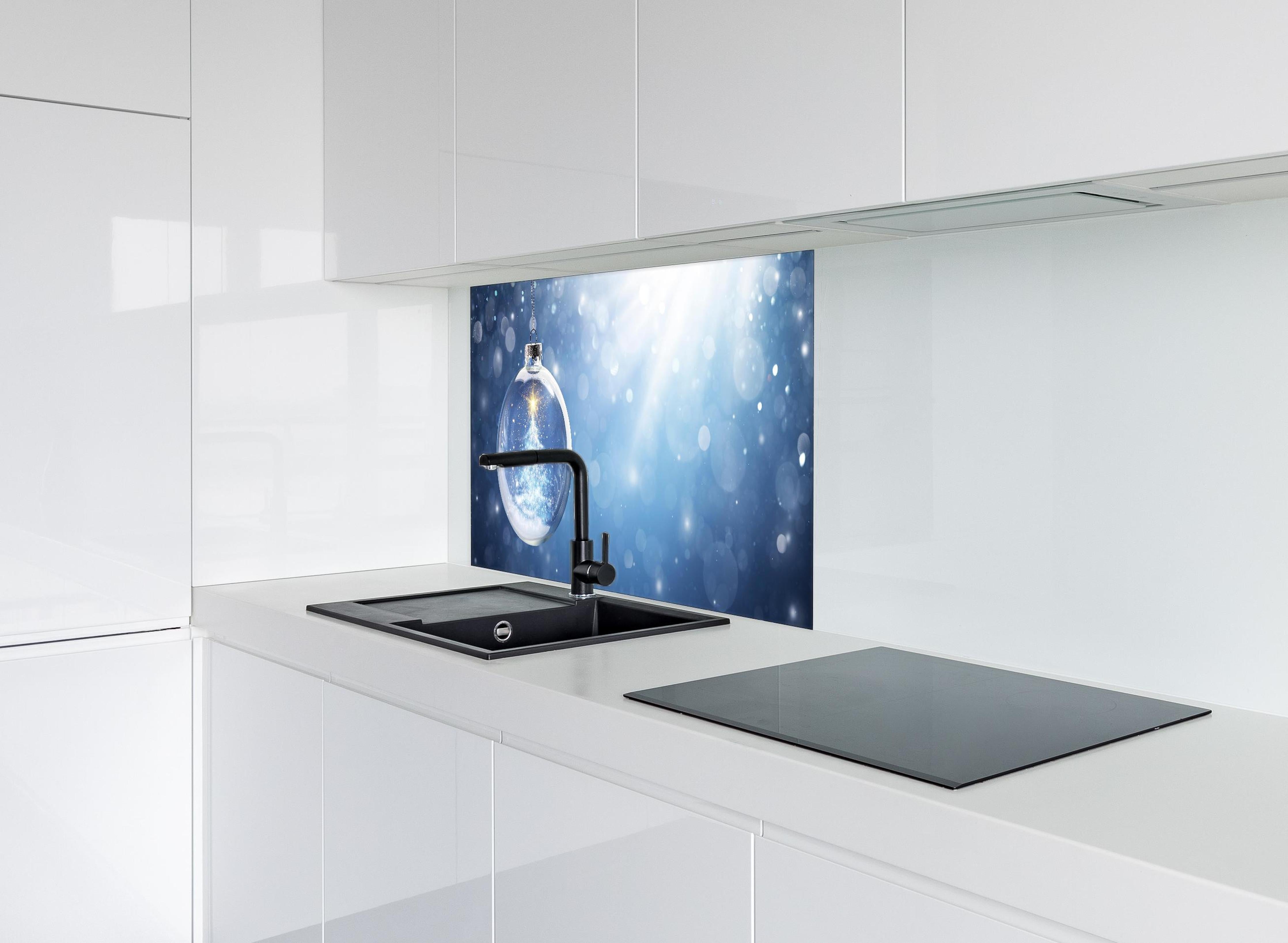 Spritzschutz - Glänzender Weihnachtsbaum in Schneekugel hinter einem Cerankochfeld zwischen Holz-Kochutensilien