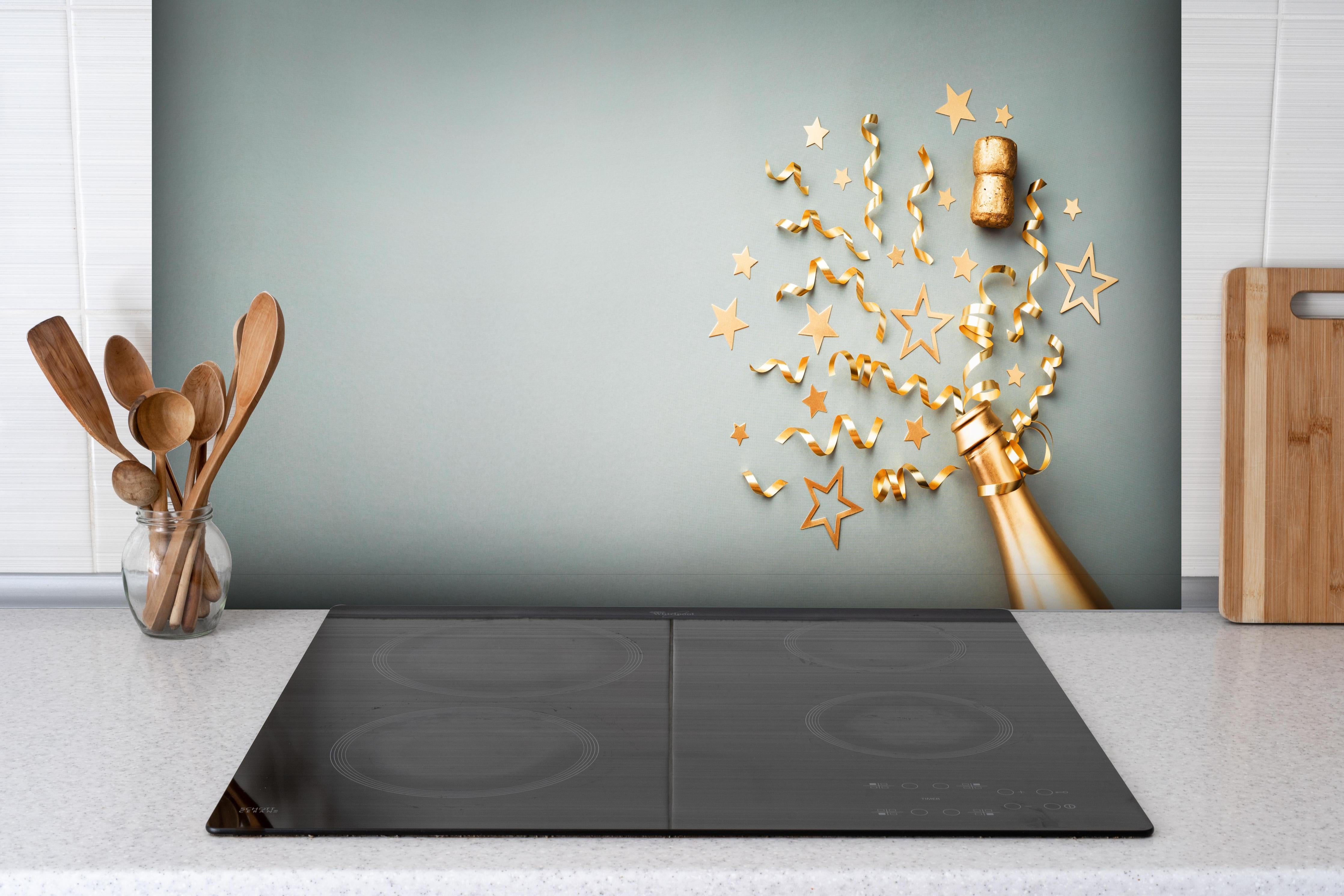 Spritzschutz - Goldene Champagnerflasche im Sylvester design hinter einem Cerankochfeld zwischen Holz-Kochutensilien