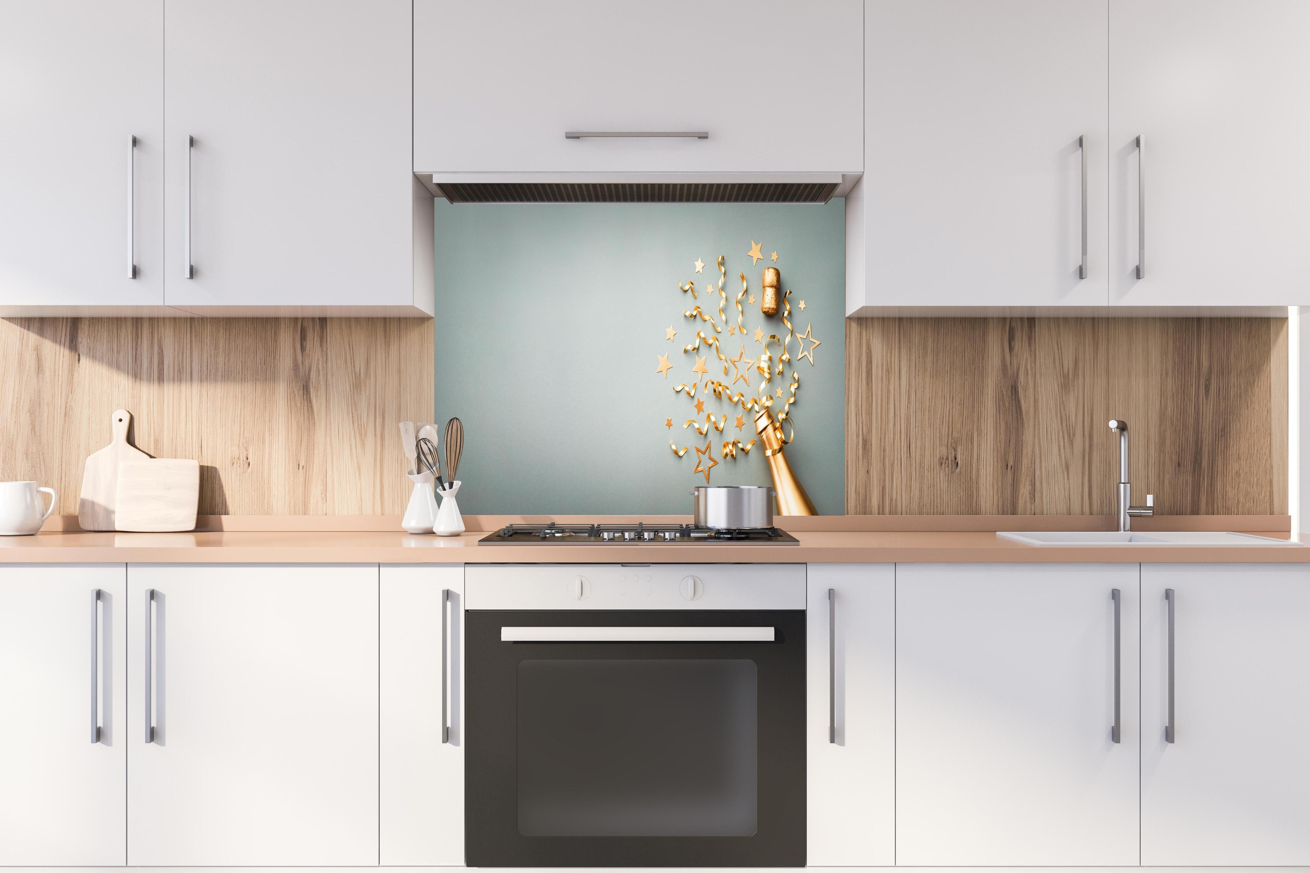 Spritzschutz - Goldene Champagnerflasche im Sylvester design hinter einem Cerankochfeld zwischen Holz-Kochutensilien