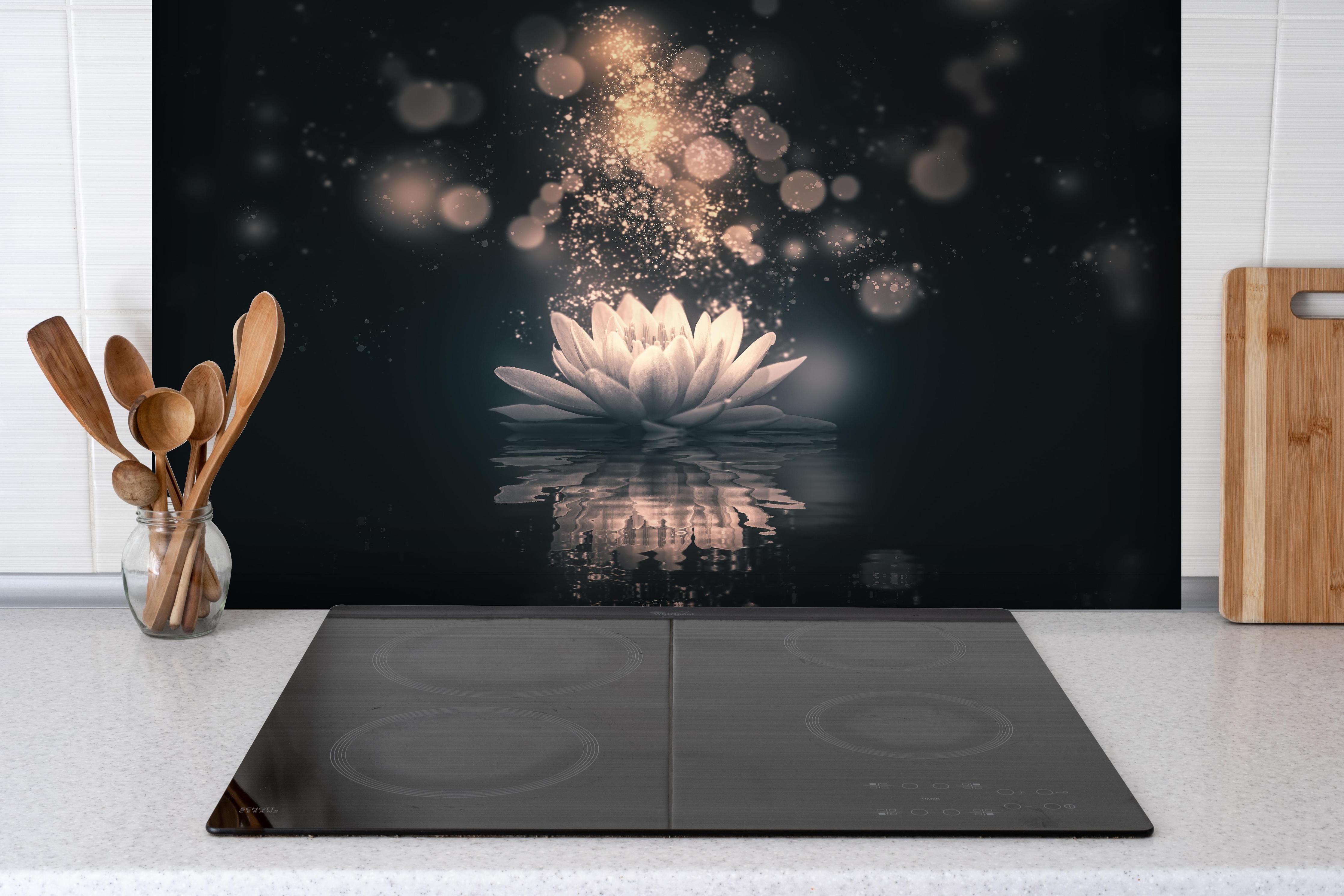 Spritzschutz - Goldene Lotusblüte auf dunklem Hintergrund hinter einem Cerankochfeld zwischen Holz-Kochutensilien