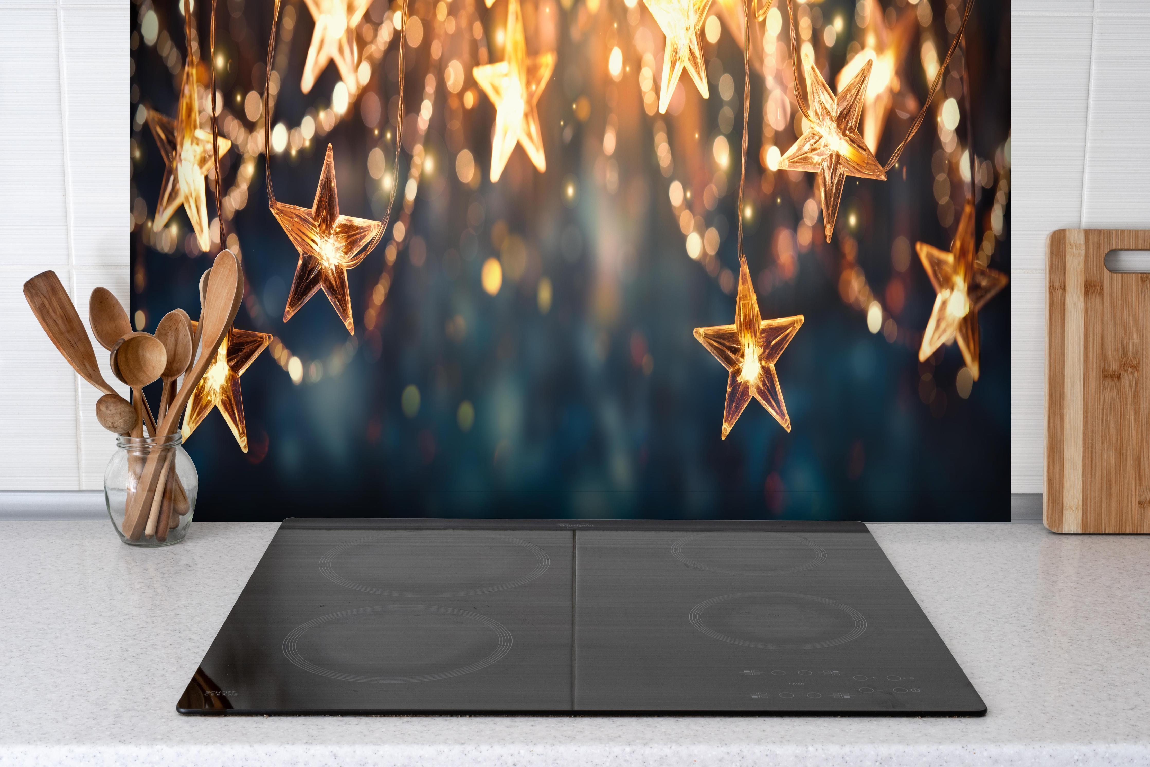 Spritzschutz - Goldene Sternen Lichterkette hinter einem Cerankochfeld zwischen Holz-Kochutensilien