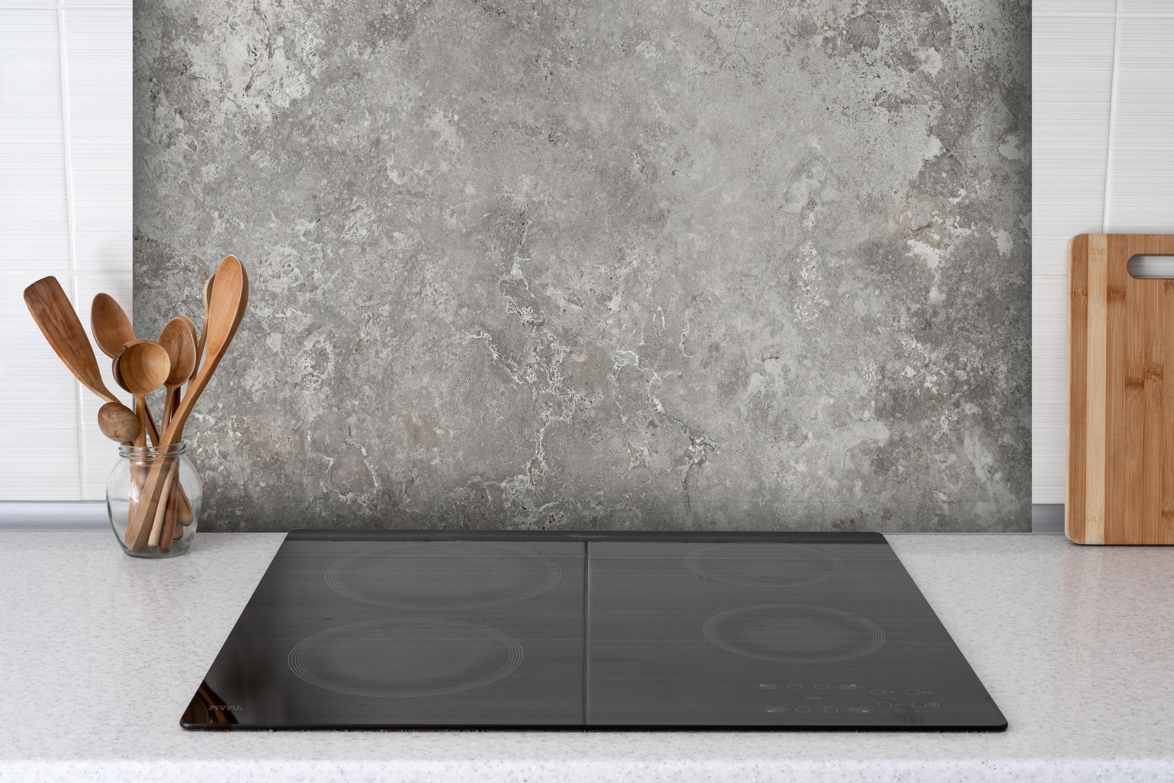 Spritzschutz - Gräulicher Zement hinter einem Cerankochfeld zwischen Holz-Kochutensilien
