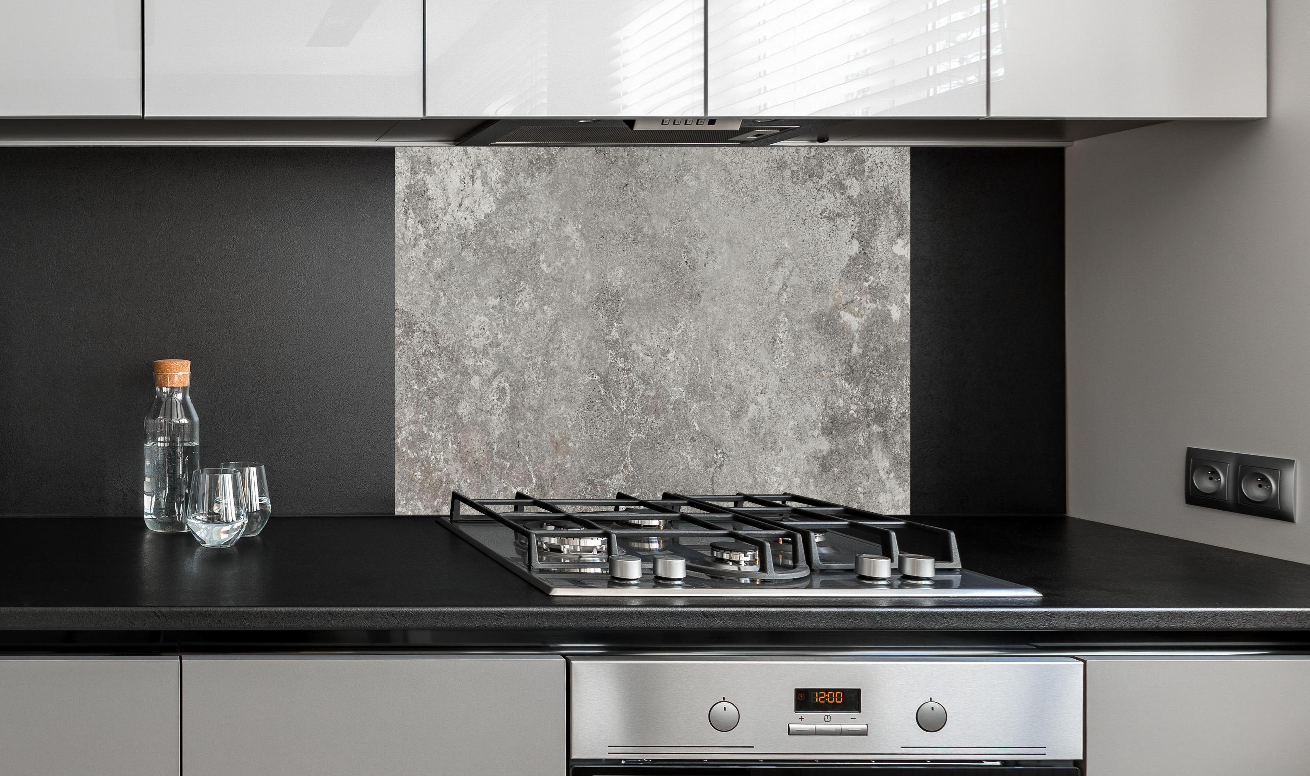 Spritzschutz - Gräulicher Zement hinter einem Cerankochfeld zwischen Holz-Kochutensilien