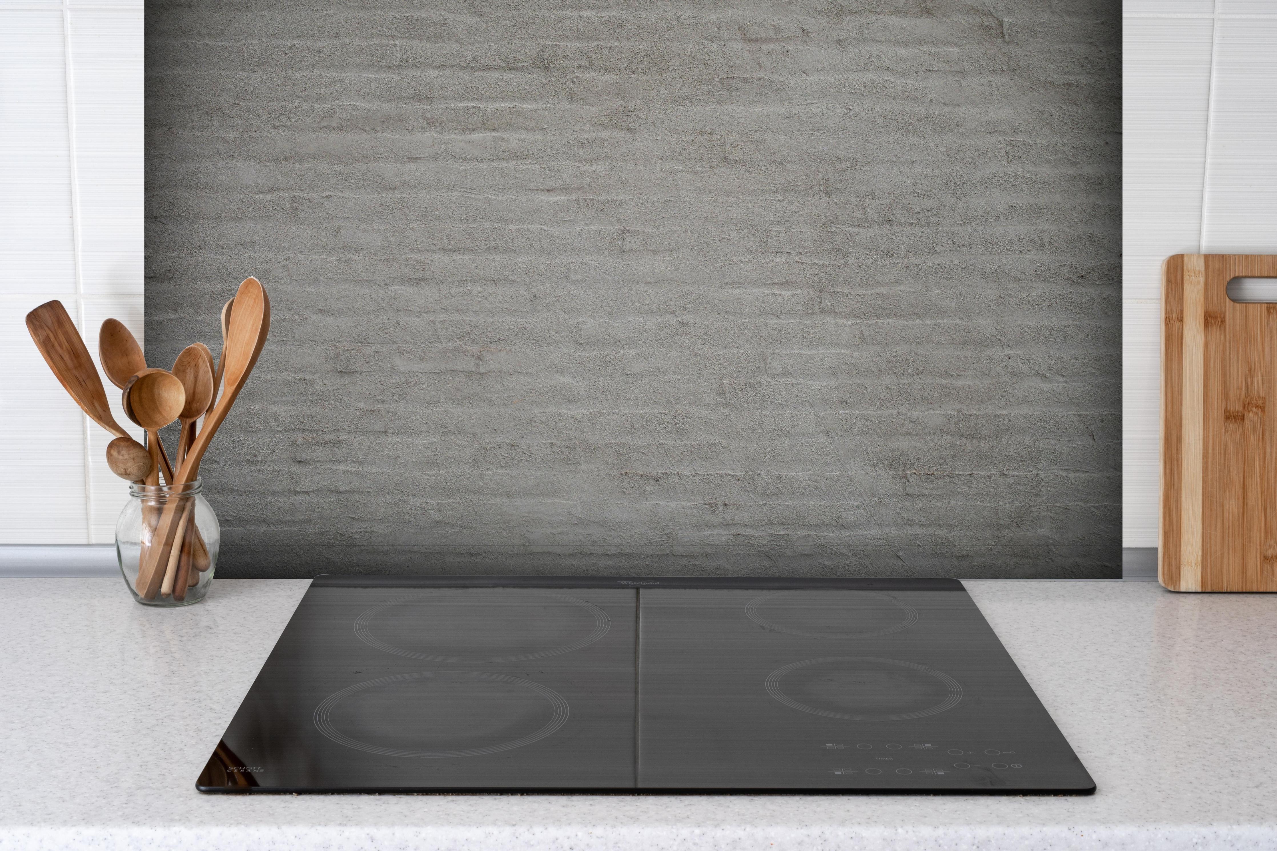 Spritzschutz - Gräuliches Mauerwerk hinter einem Cerankochfeld zwischen Holz-Kochutensilien