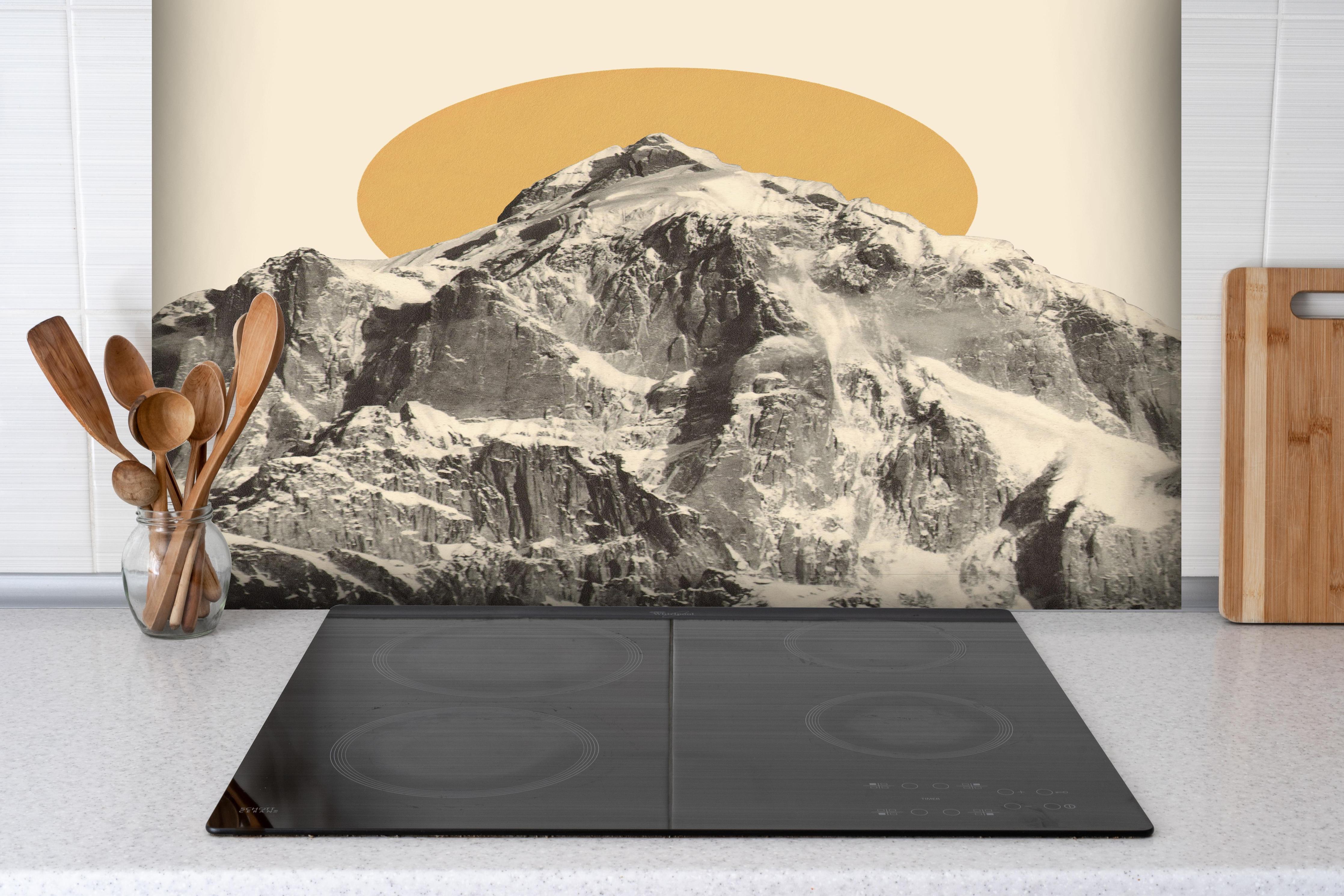 Spritzschutz - Grafisches Bergmotiv mit Sonne im Hintergrund hinter einem Cerankochfeld zwischen Holz-Kochutensilien