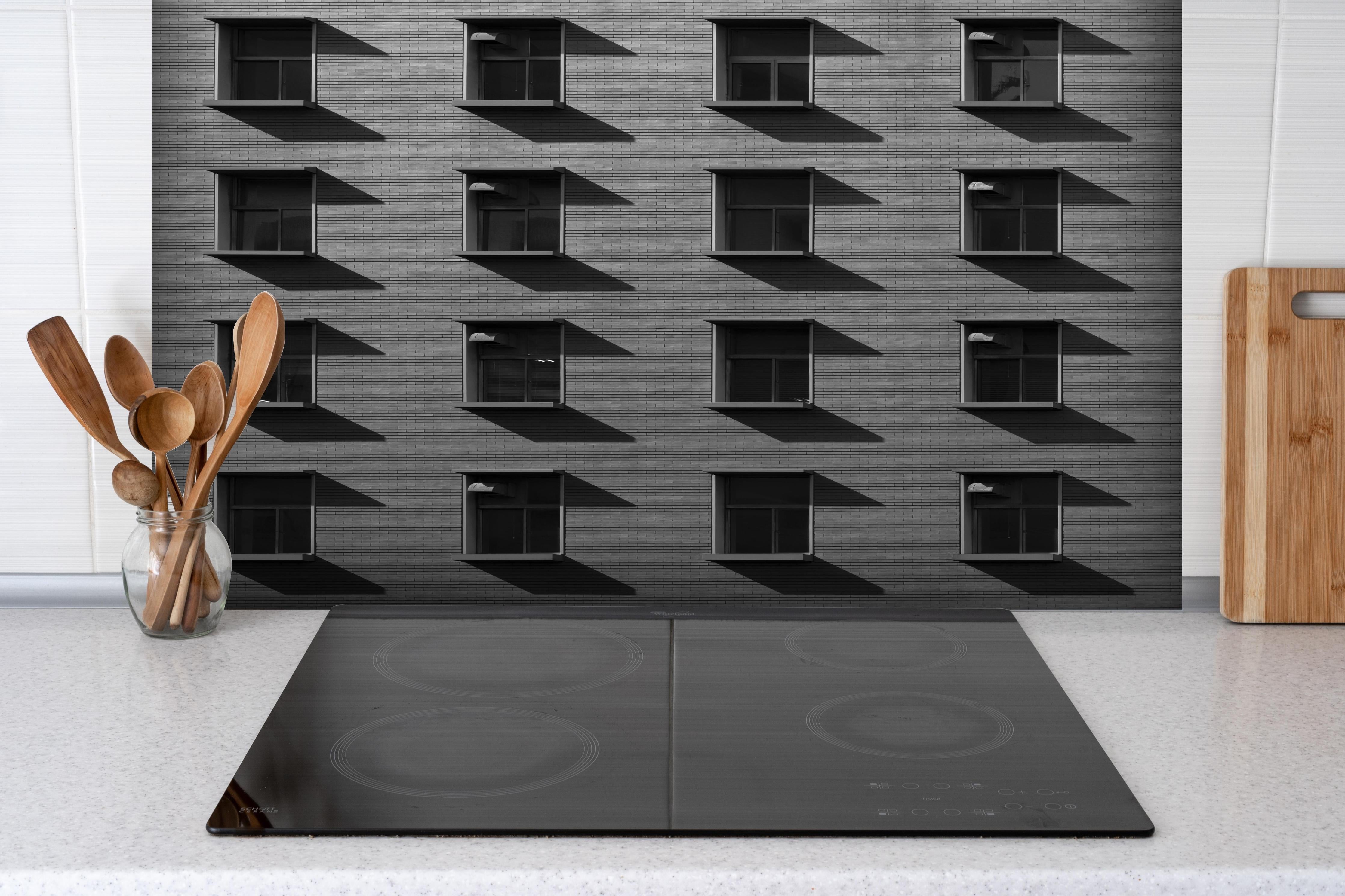Spritzschutz - Grafisches graues Gebäudefassaden-Muster hinter einem Cerankochfeld zwischen Holz-Kochutensilien