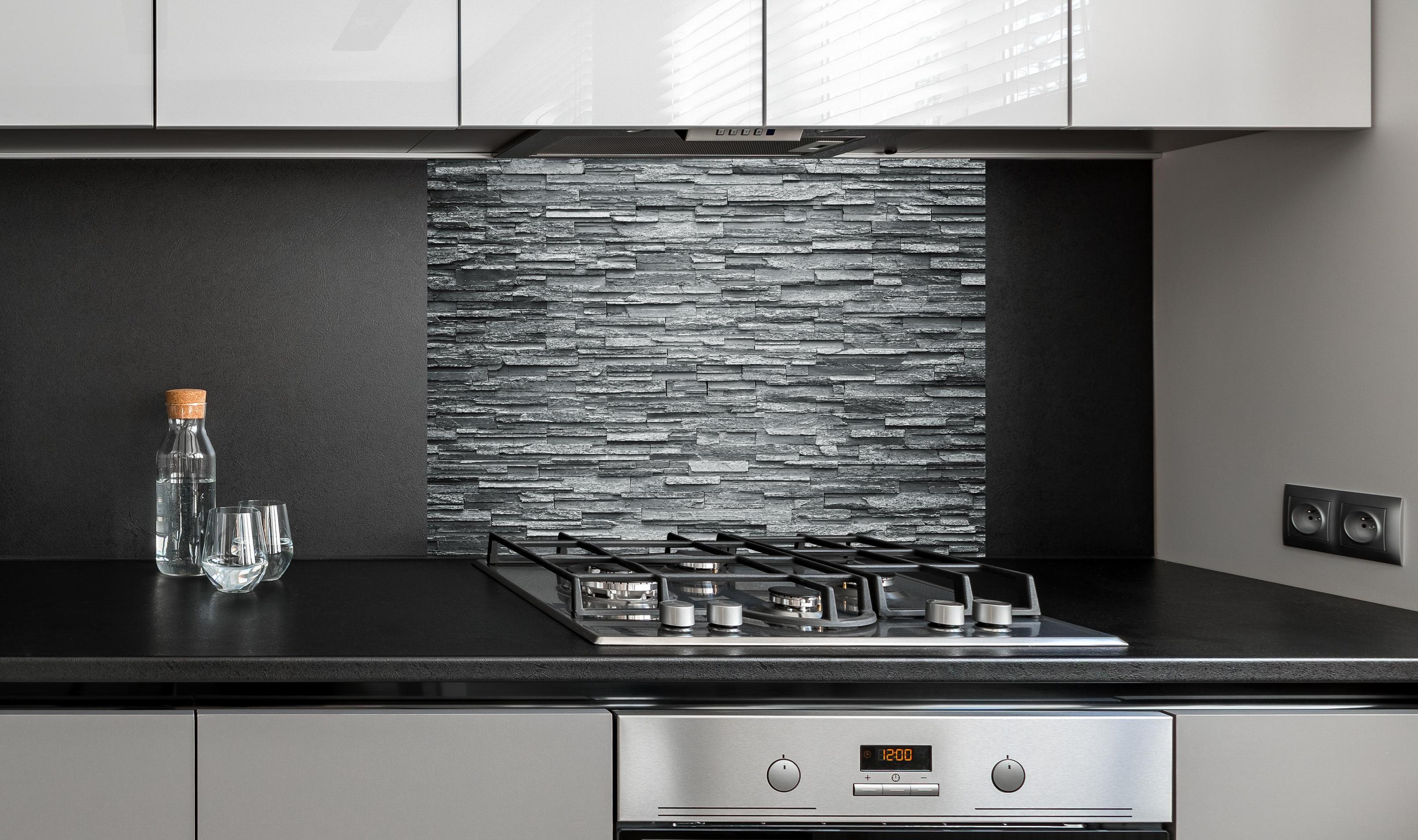 Spritzschutz - Graue Steinziegel hinter einem Cerankochfeld zwischen Holz-Kochutensilien