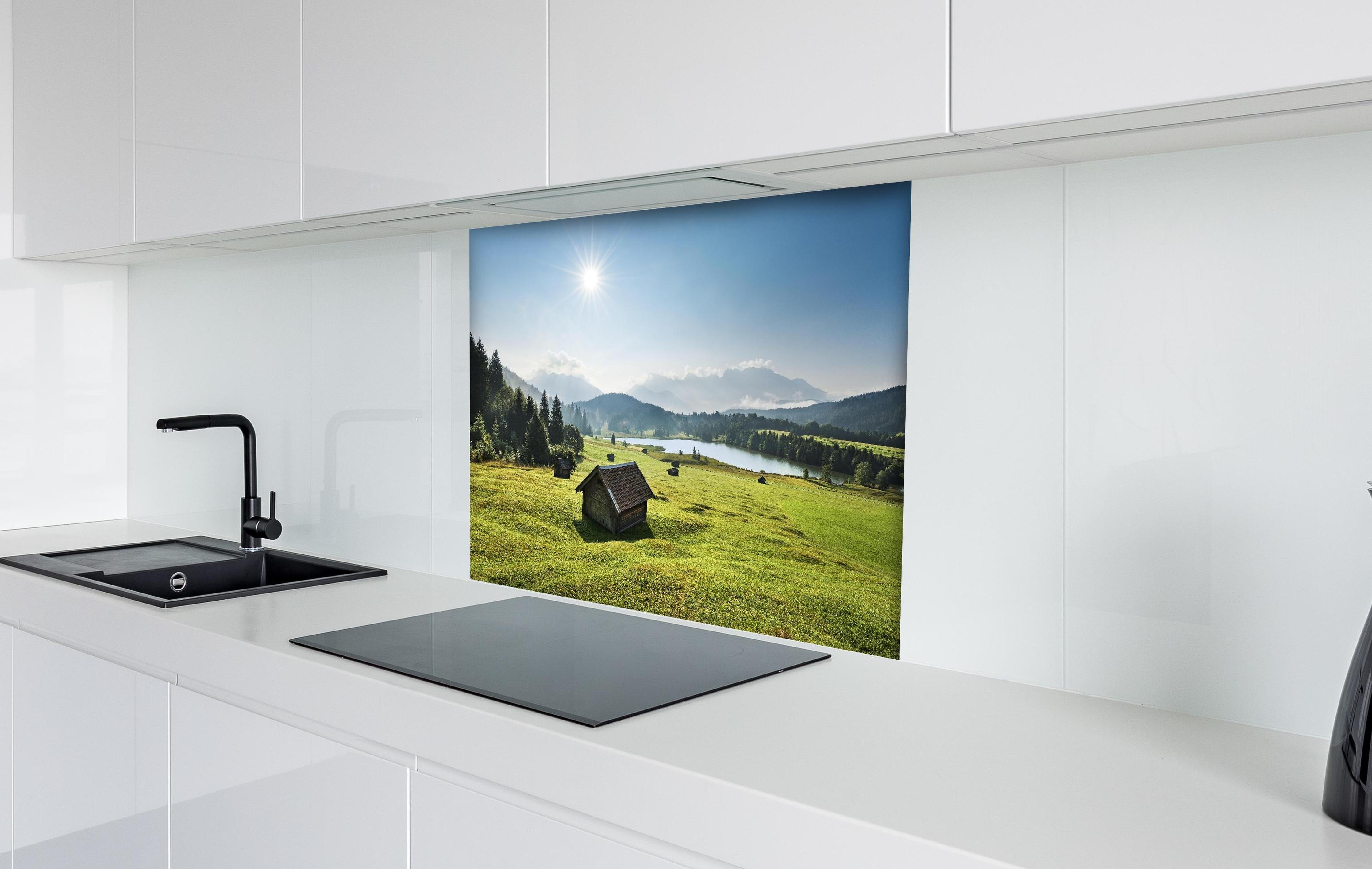 Spritzschutz - Grüne Alpenwiese, Berge und See im Sonnenschein hinter einem Cerankochfeld zwischen Holz-Kochutensilien