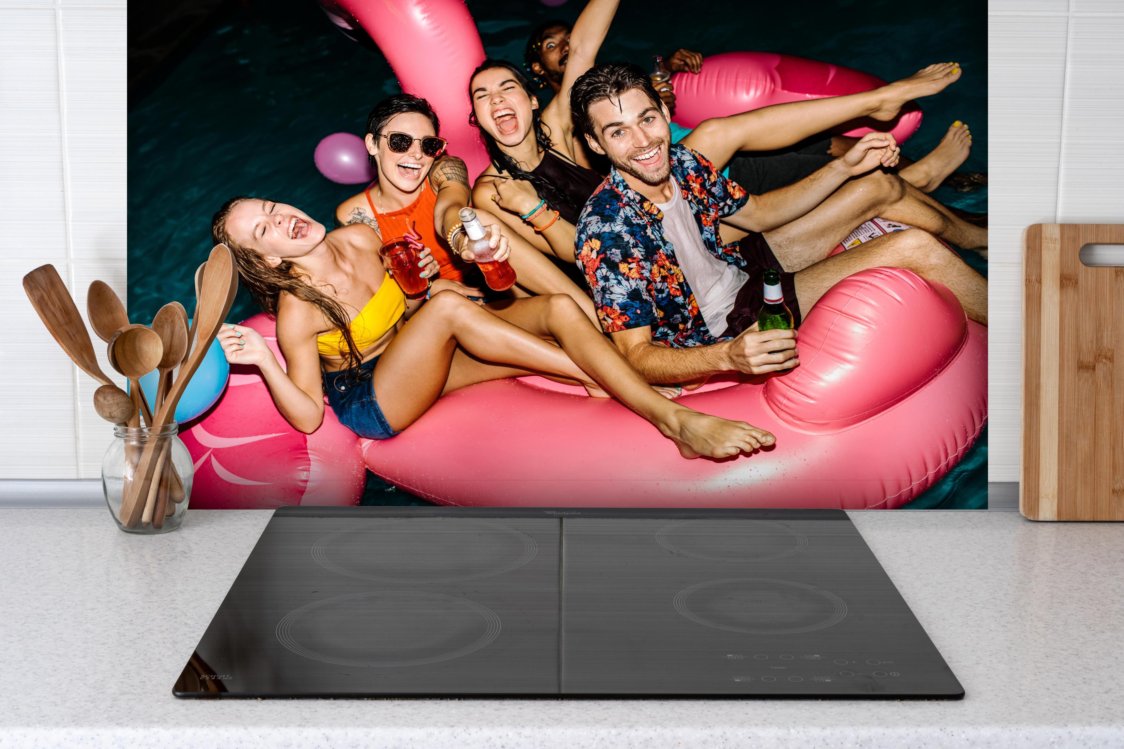 Spritzschutz - Gruppe von Leuten in Partystimmung hinter einem Cerankochfeld zwischen Holz-Kochutensilien