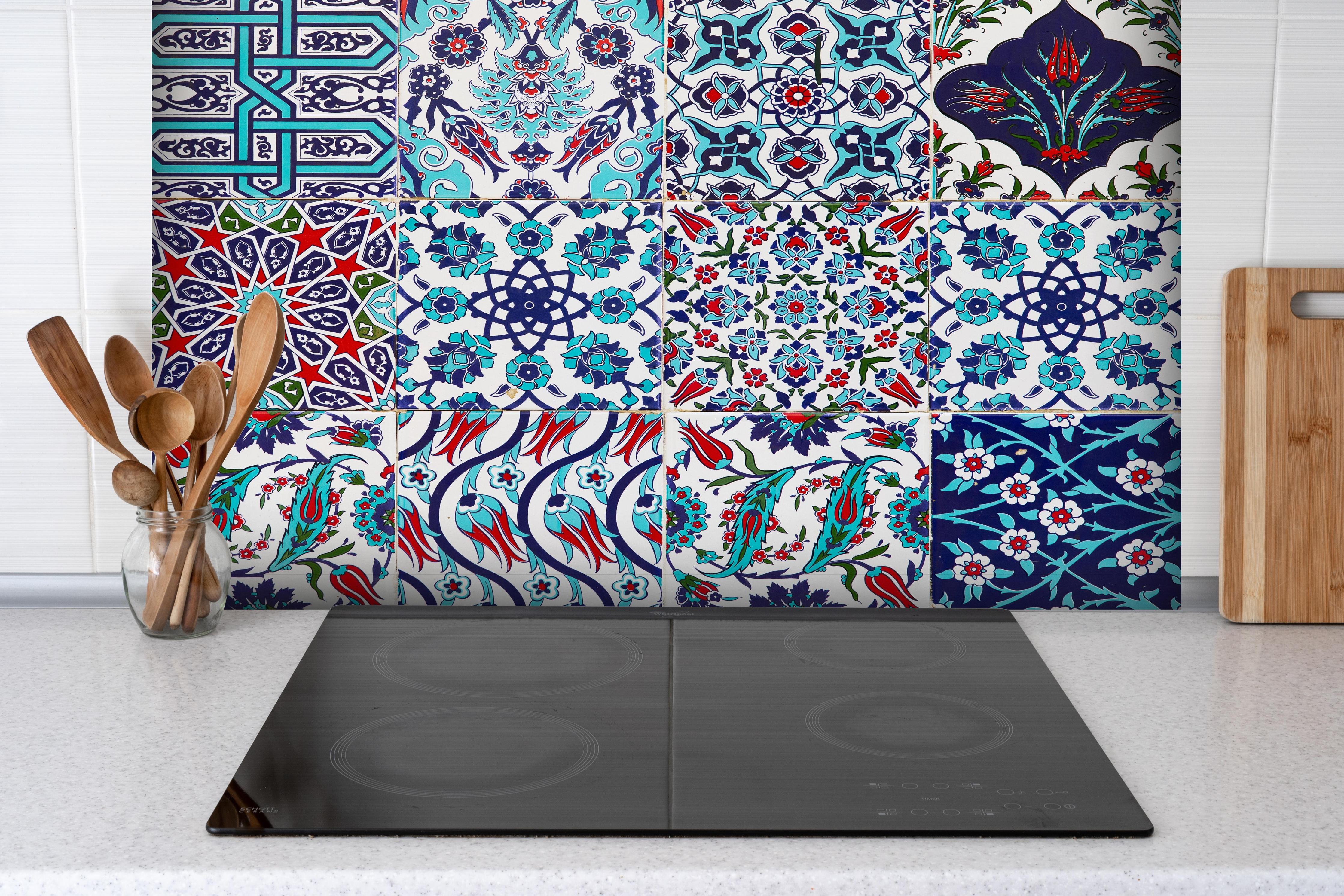 Spritzschutz - Handgefertigte osmanische Fliesen Türkisblau hinter einem Cerankochfeld zwischen Holz-Kochutensilien
