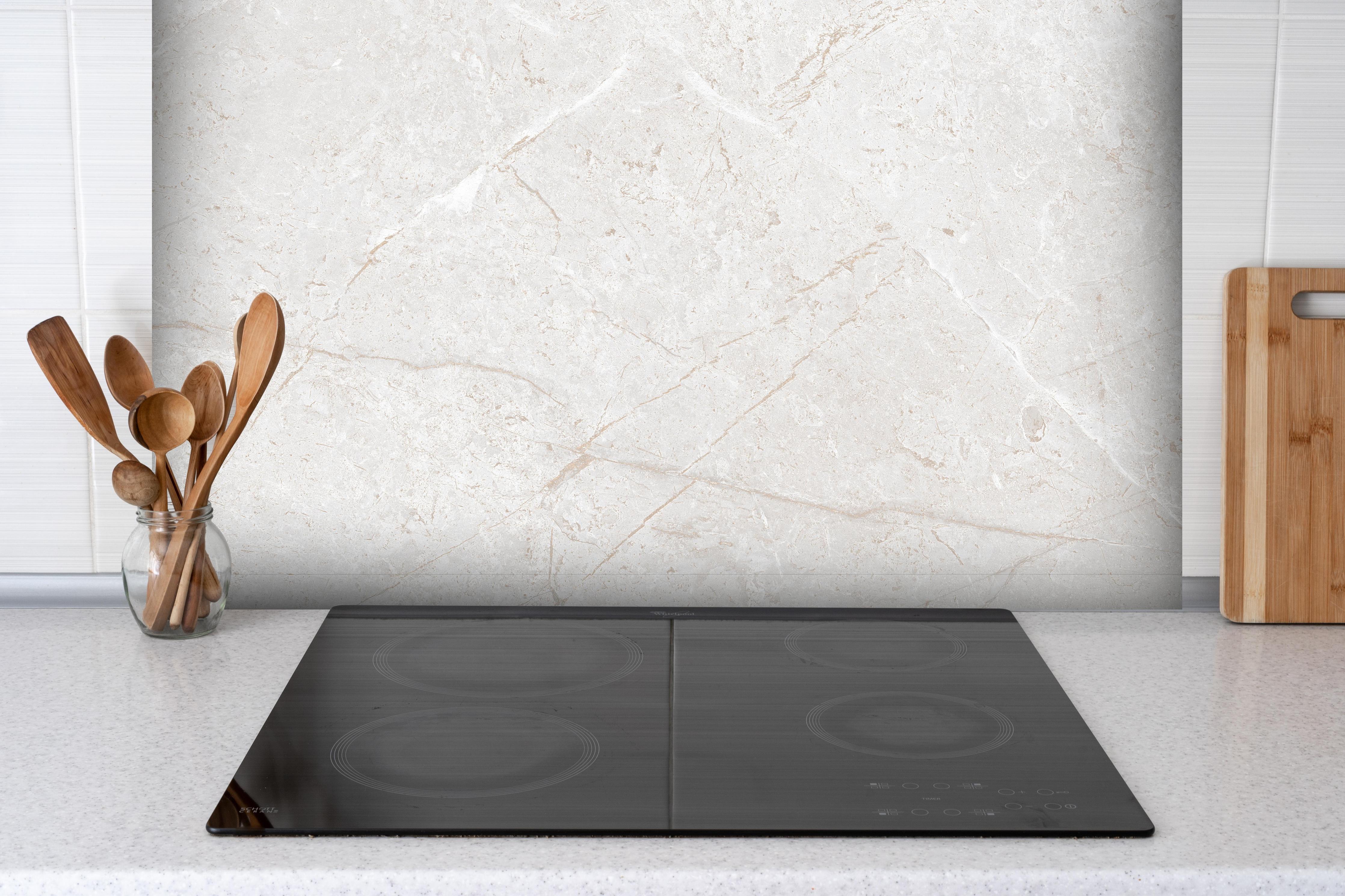 Spritzschutz - Heller Marmor Hintergrund hinter einem Cerankochfeld zwischen Holz-Kochutensilien