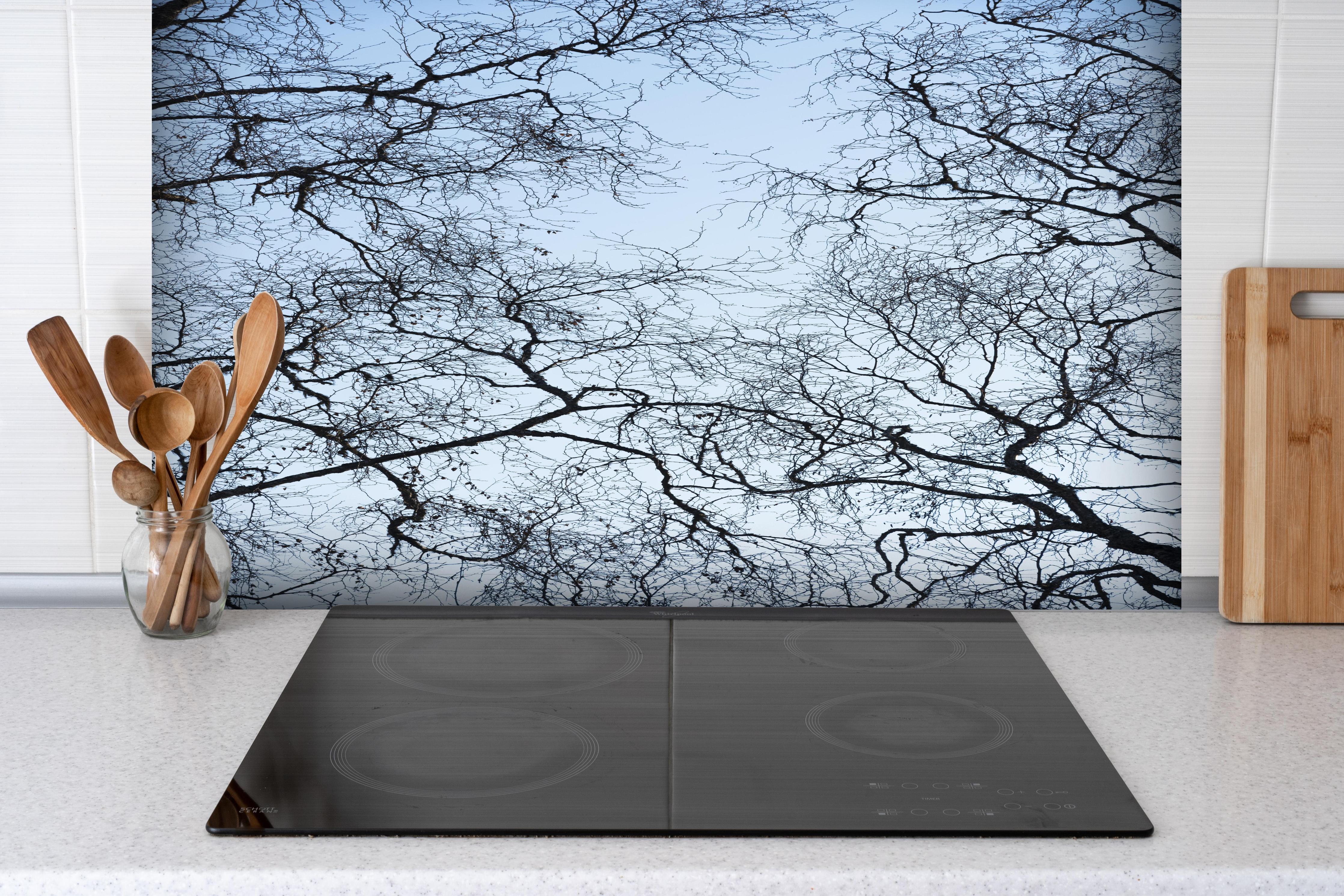 Spritzschutz - Himmelblick durch verzweigte Baumkronen hinter einem Cerankochfeld zwischen Holz-Kochutensilien