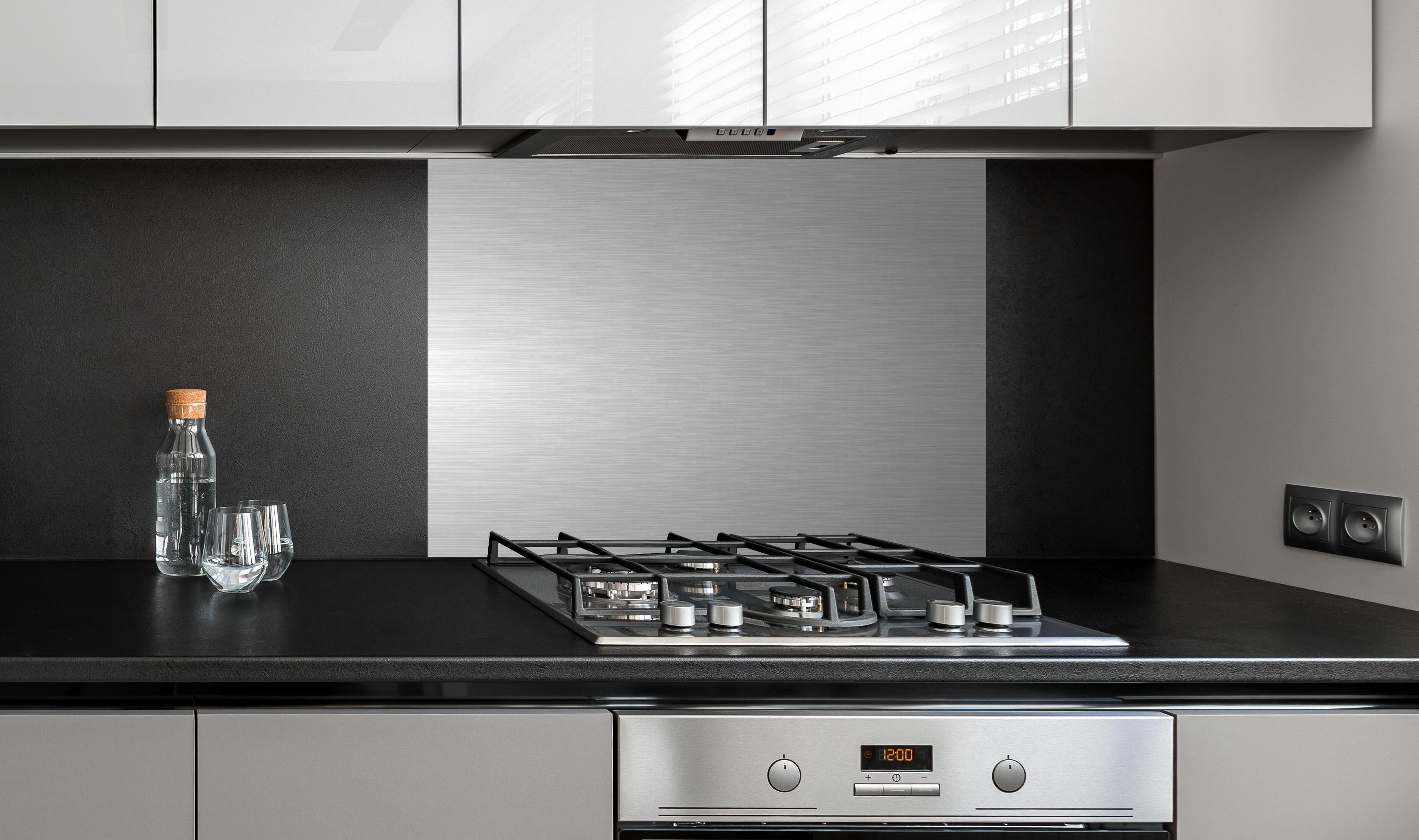 Spritzschutz - Hochwertige gebürstete Silber-Metallstruktur hinter einem Cerankochfeld zwischen Holz-Kochutensilien